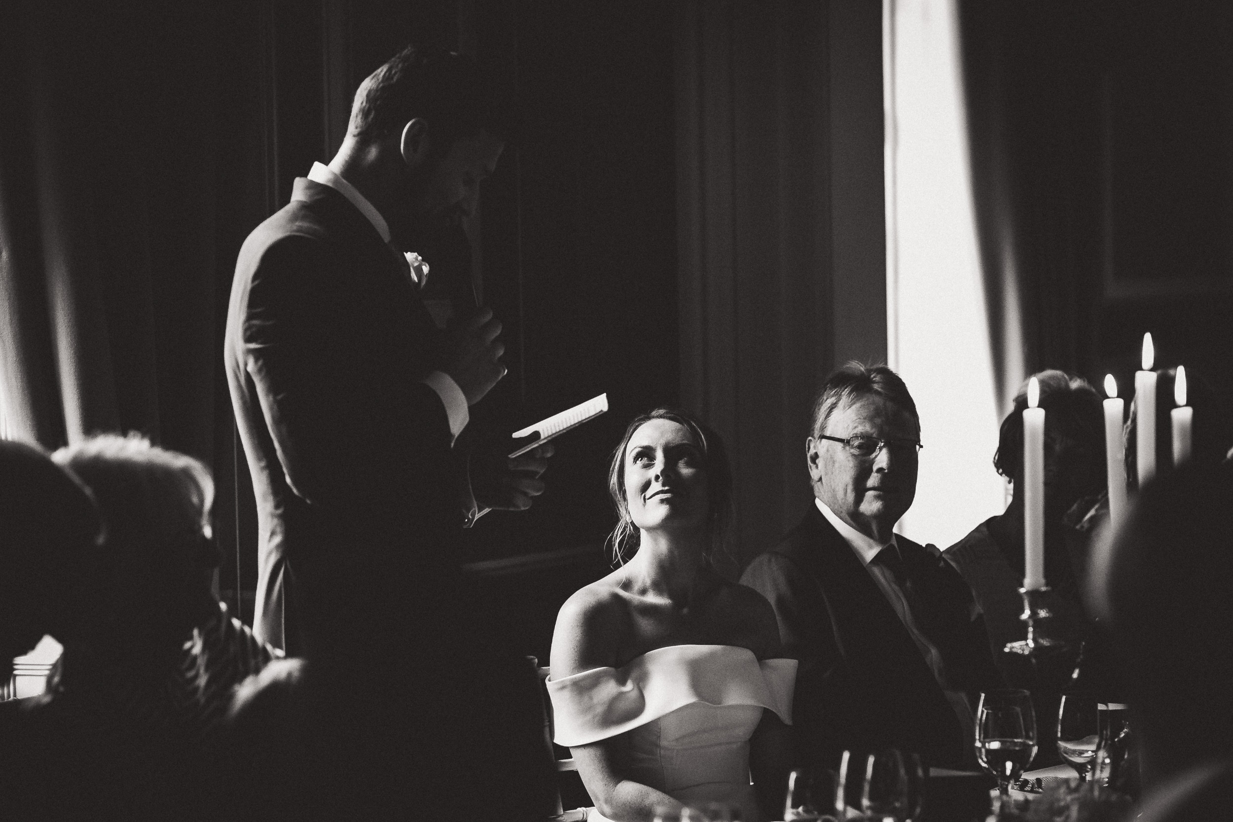 A wedding photographer captures a black and white wedding photo of a man giving a speech.