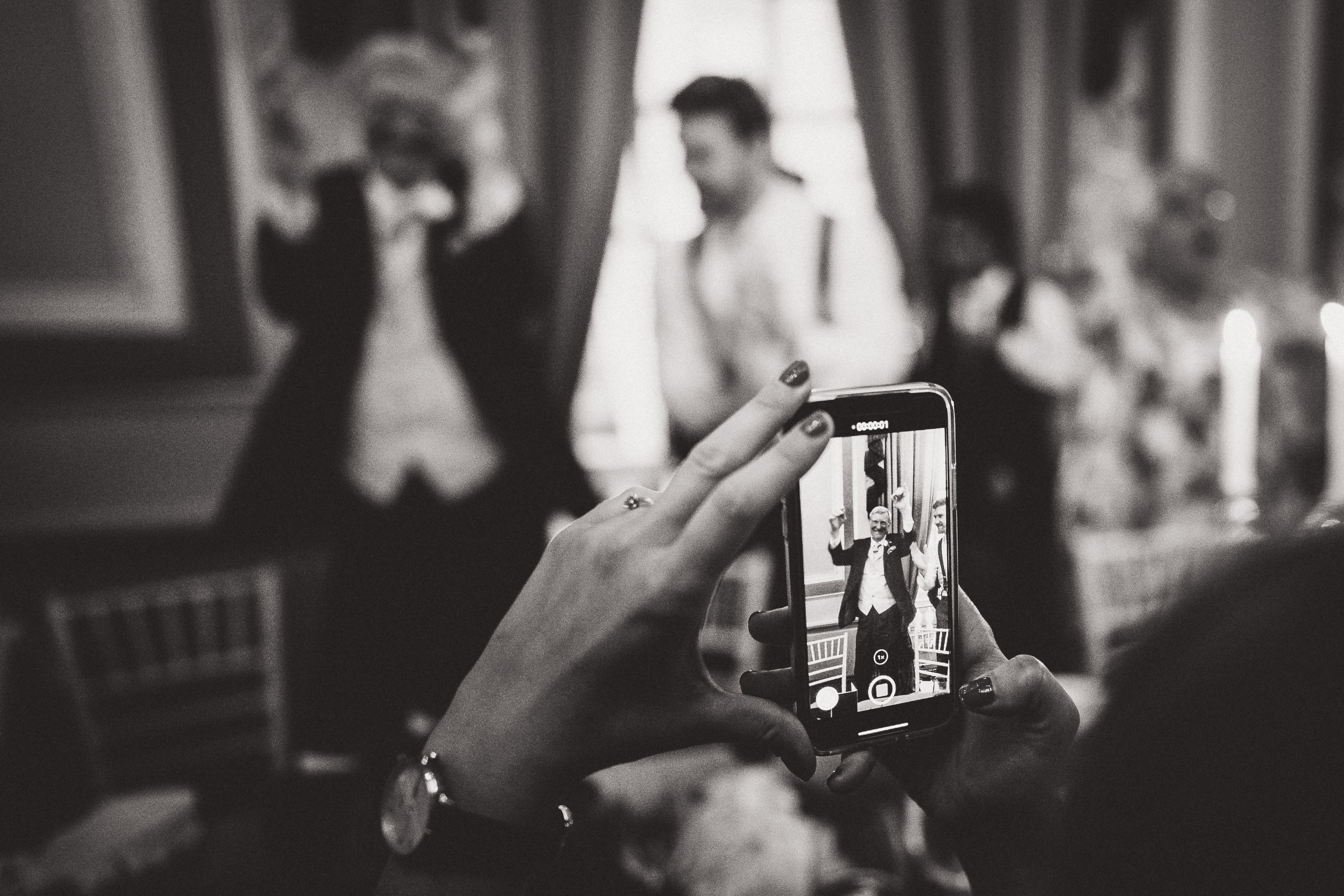 A wedding photographer capturing candid moments of the bride and groom using their cell phone.