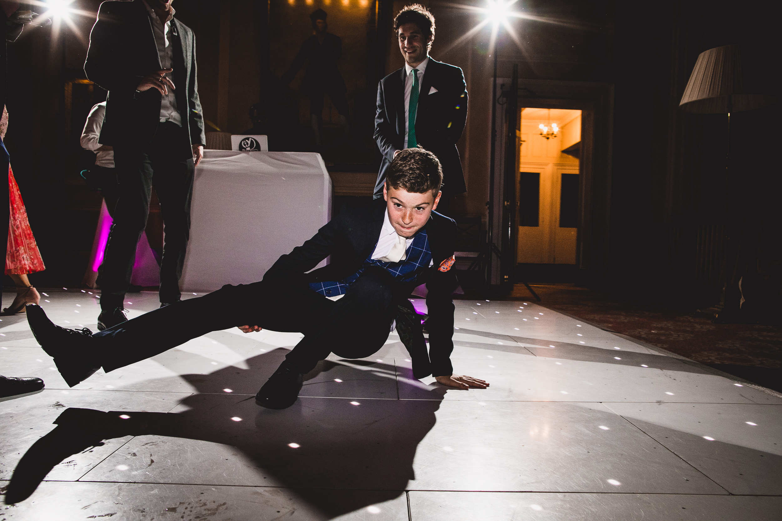 A man in a suit, captured by a wedding photographer, dancing on the wedding floor.
