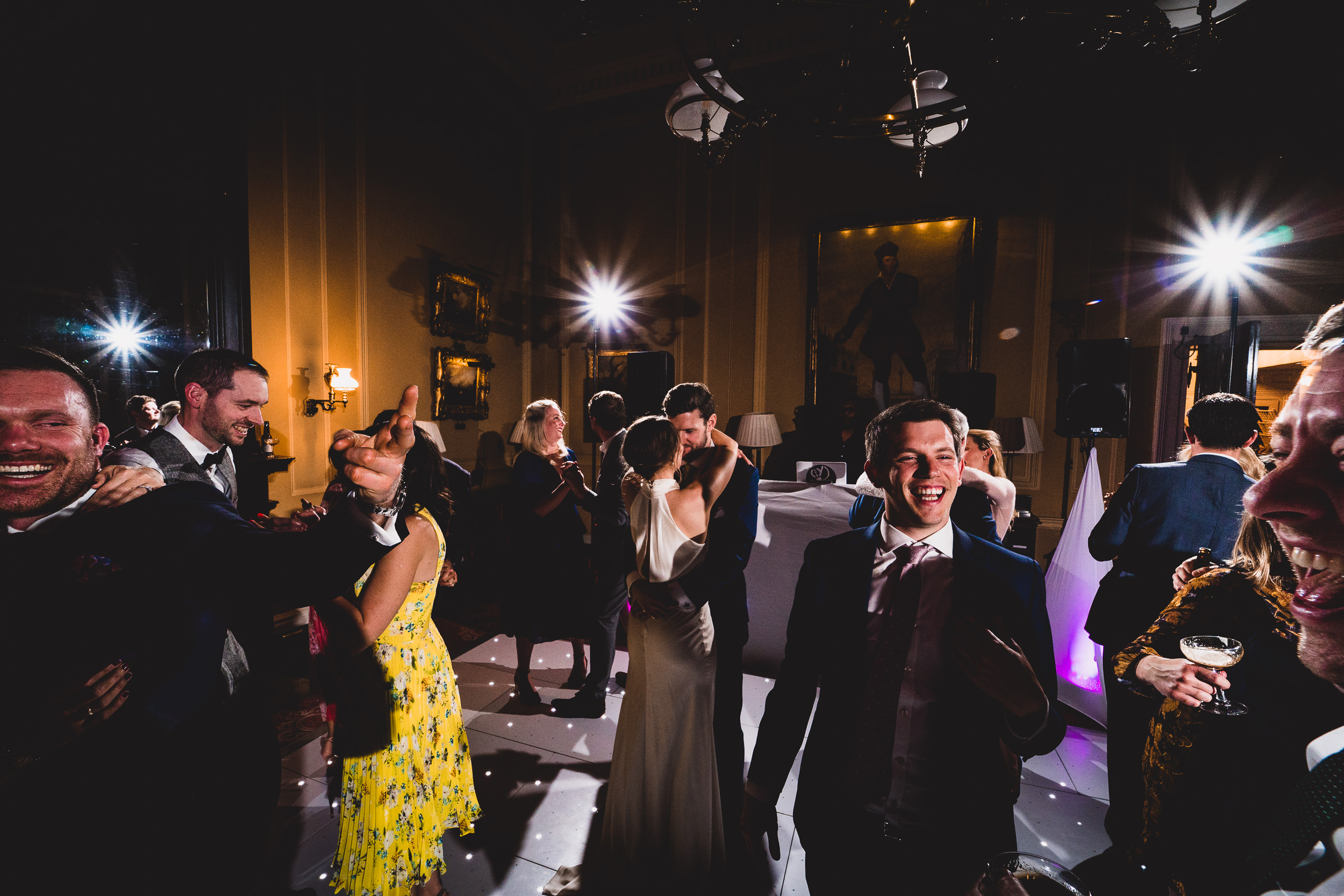 A wedding photographer capturing the groom and a group of people dancing at a wedding reception.