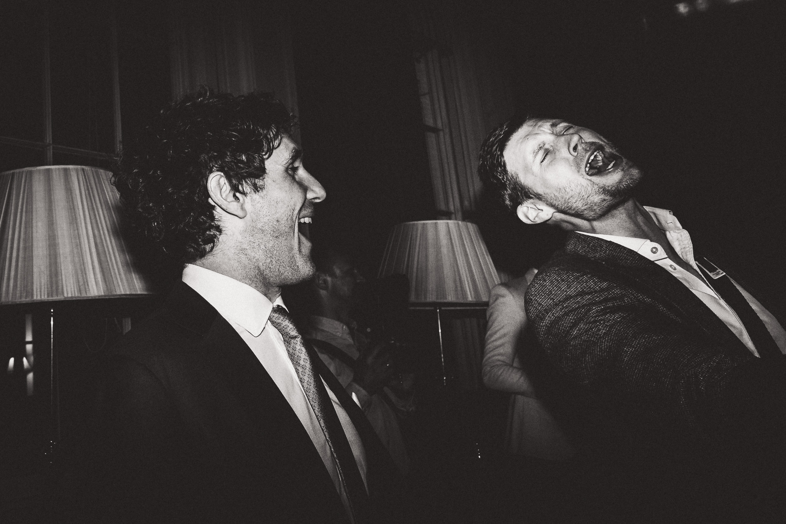 A groom and a wedding photographer capturing humorous moments in a dimly lit room.