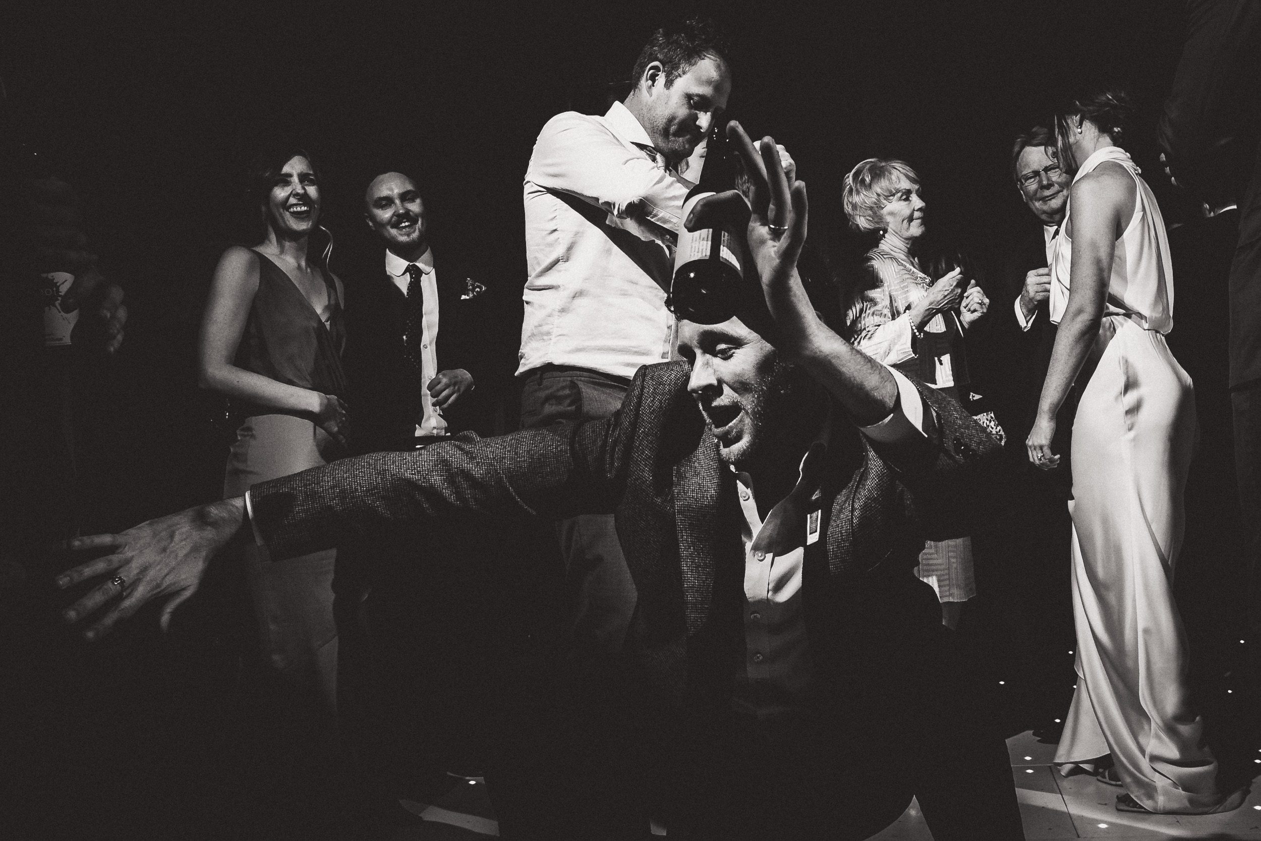 Black and white photo of a groom dancing with a group of people at a wedding.