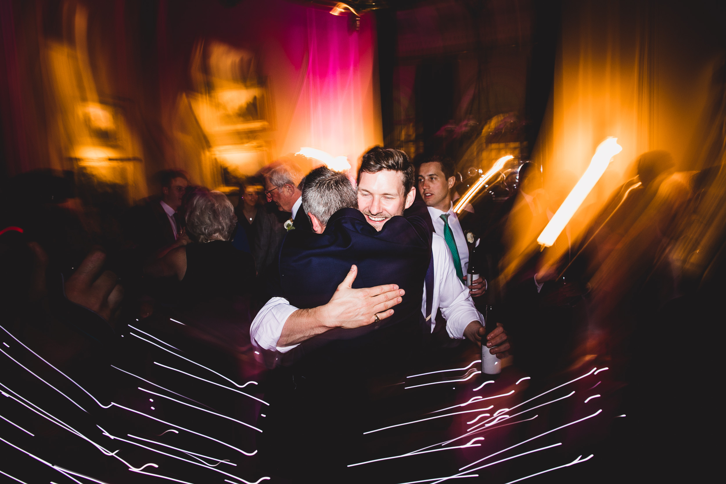 The groom is hugging another man at a wedding party.