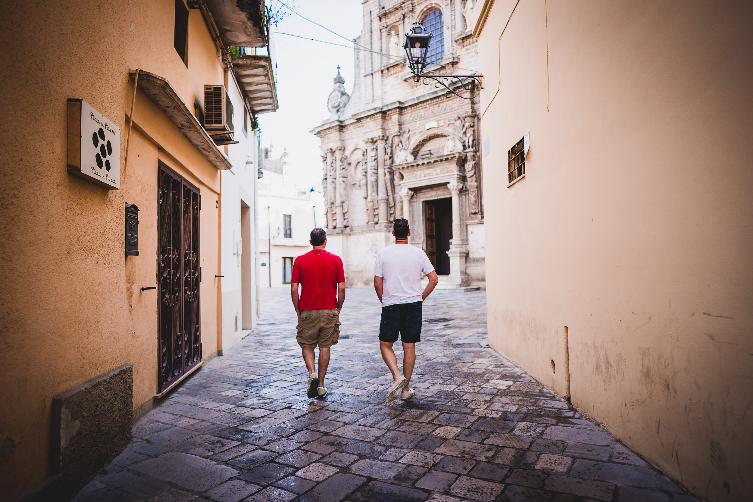 Two men walking down a cobblestone street during a wedding.