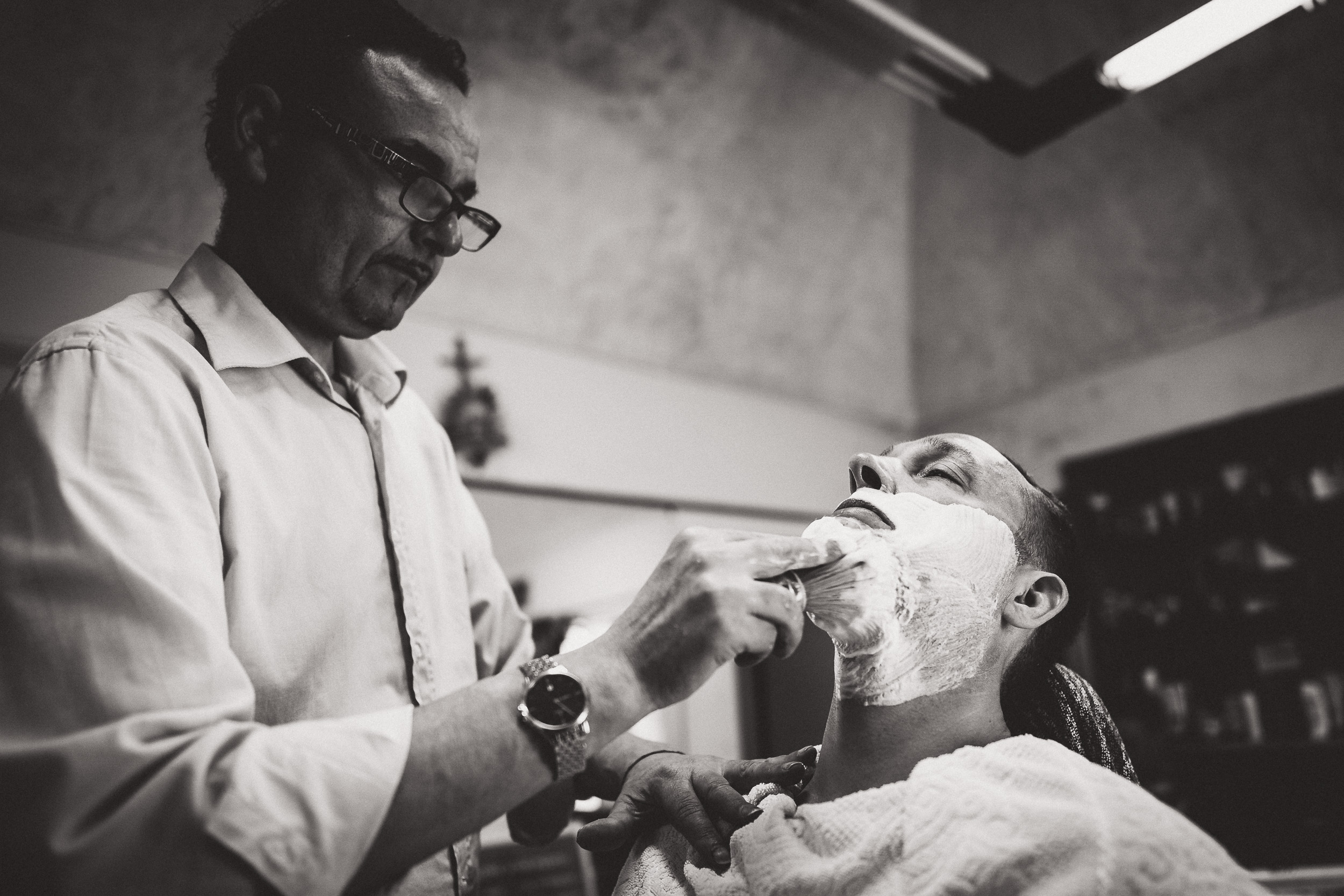 A groom shaving his beard in a barber shop before the wedding photo.