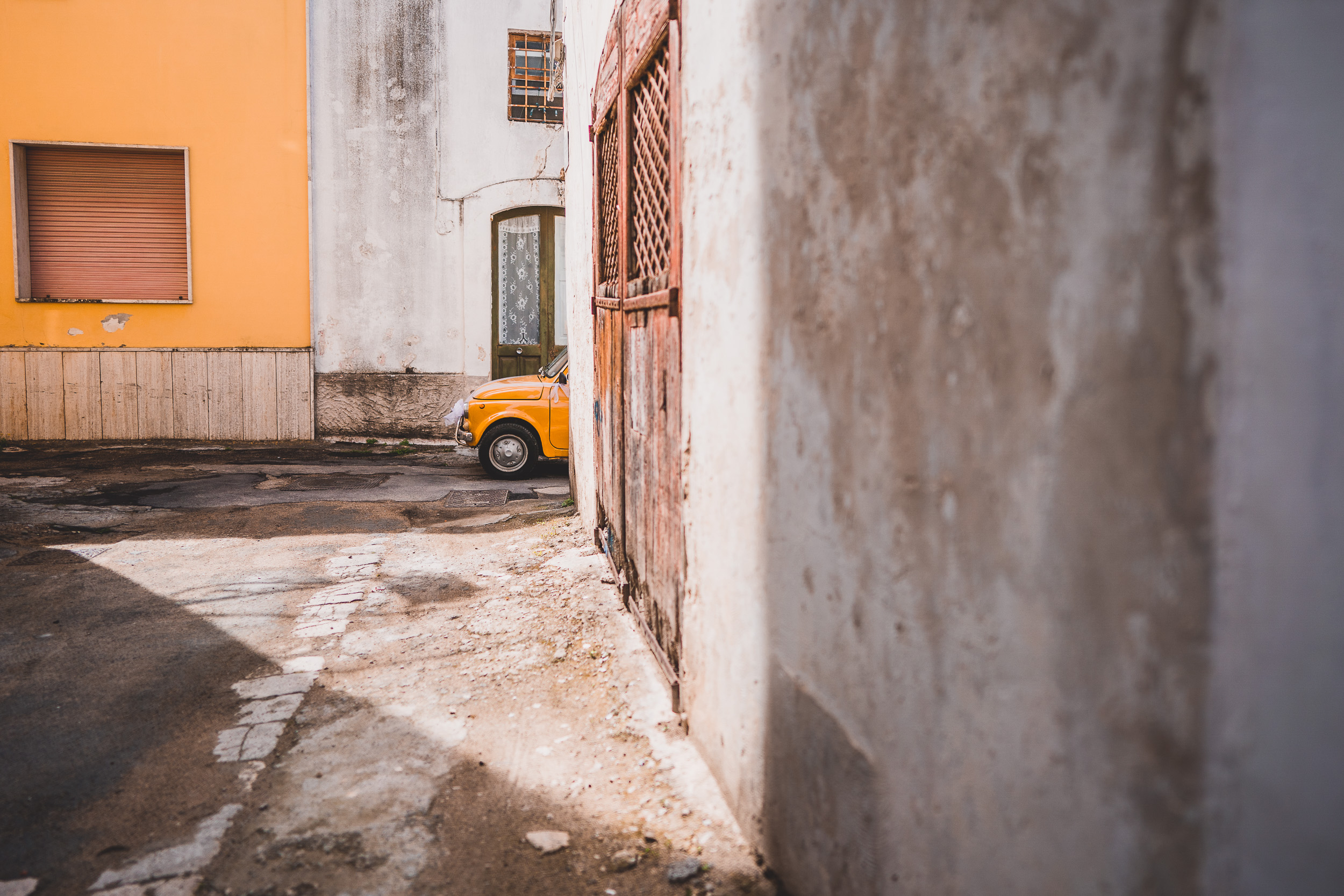 A yellow car parked in a narrow alley, providing the perfect backdrop for a bride's wedding photo.