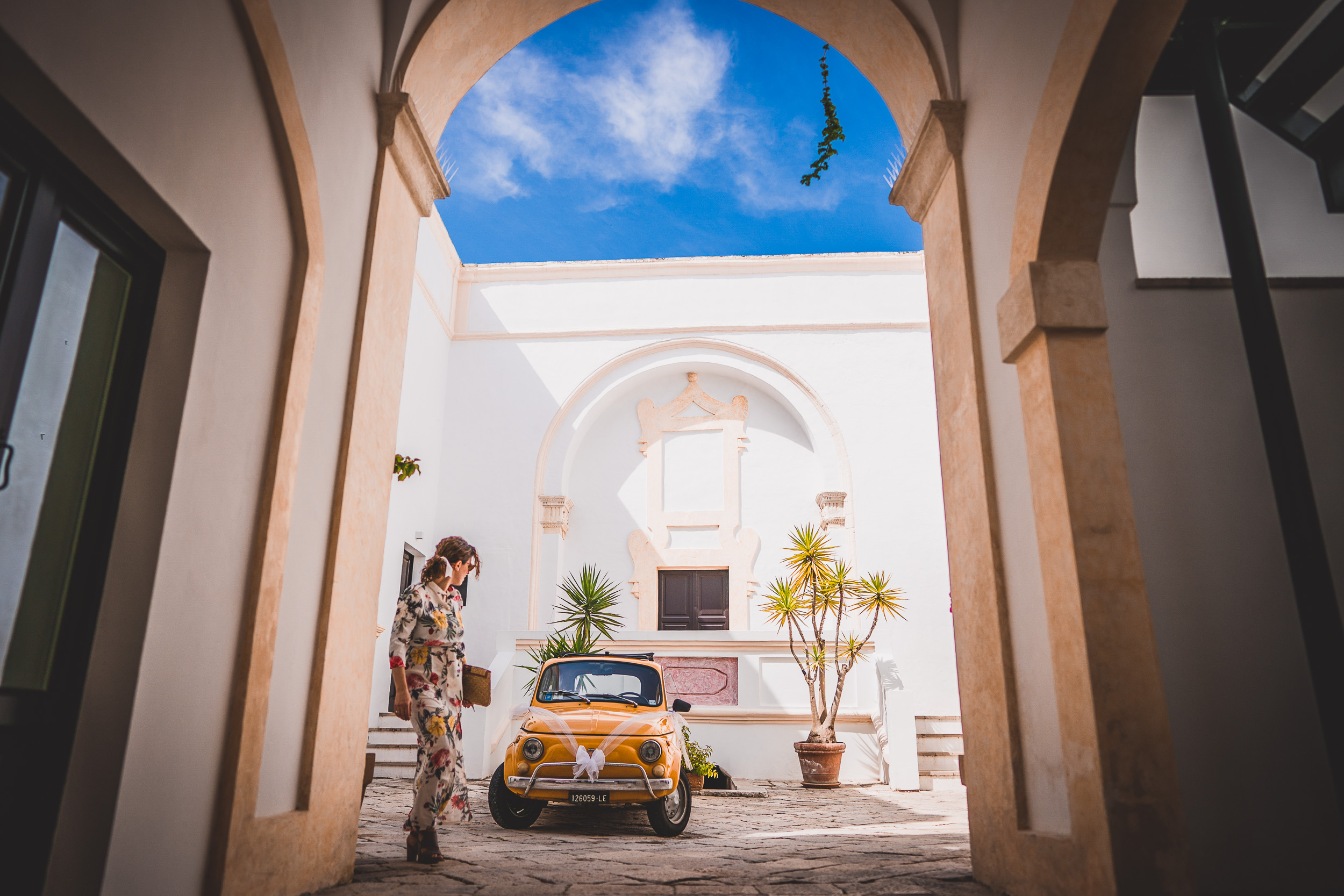 A bride posing next to an old car in an alleyway for her wedding photo.