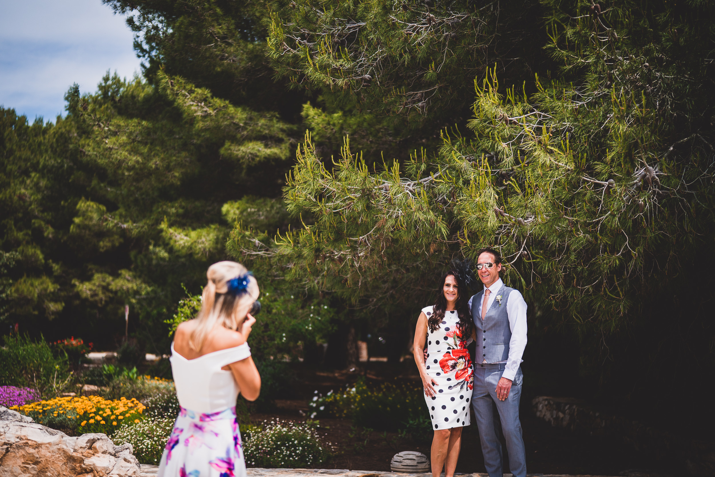 A groom capturing a wedding photo in front of a tree.