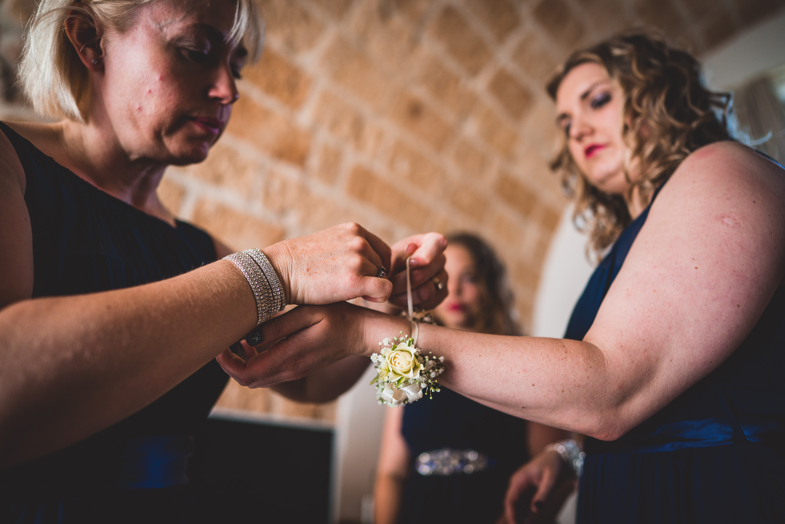 Two bridesmaids assisting each other with a flower at a wedding.