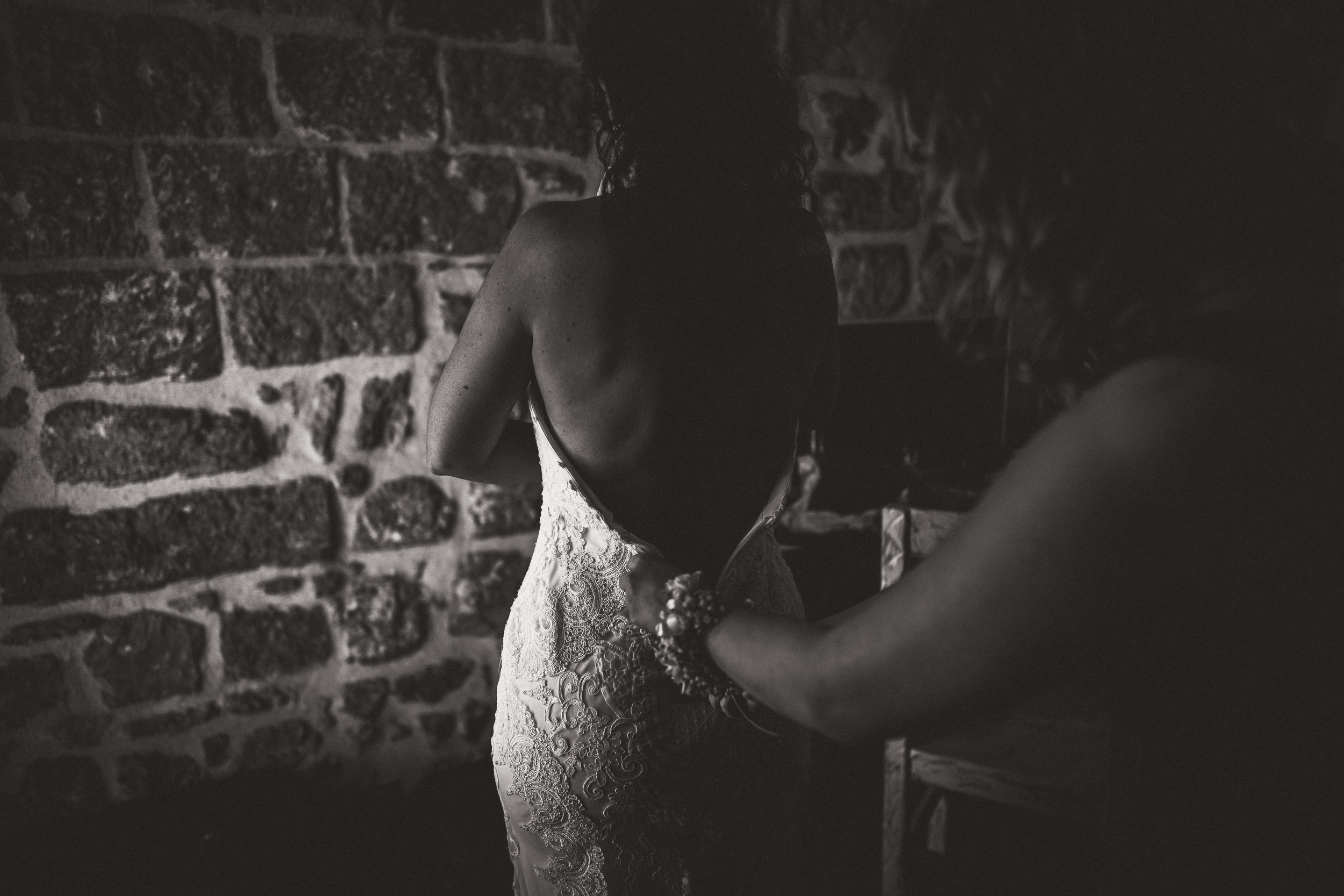 A bride is preparing for her wedding, captured by a wedding photographer in a dimly lit room.