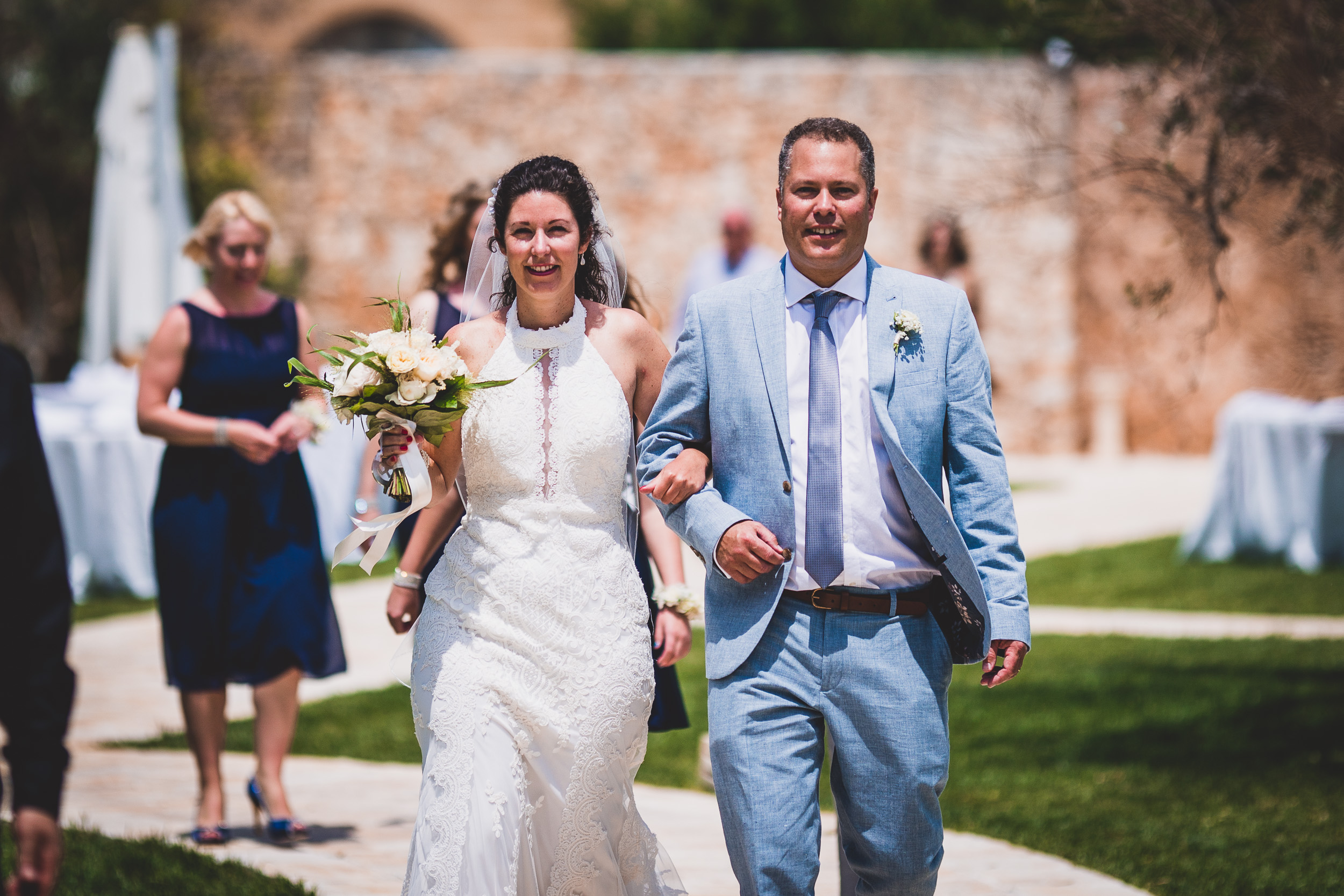 A wedding photographer capturing a bride and groom walking down a path.