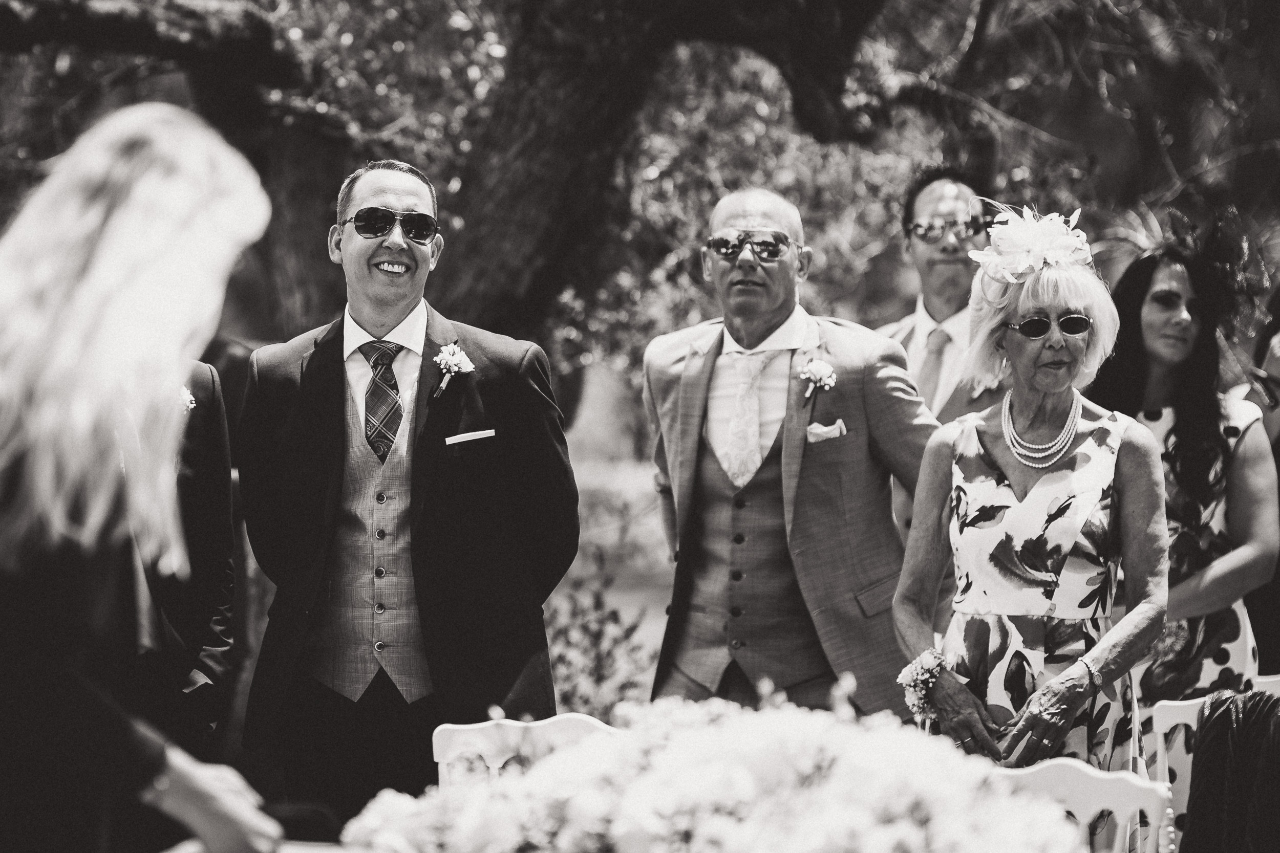 A black and white wedding photo capturing the bride and groom with a group of people.