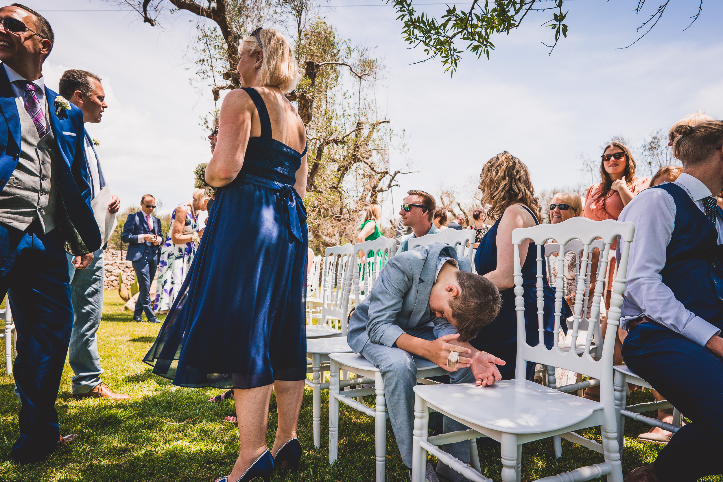 A groom is lounging on a white chair for a wedding photo.