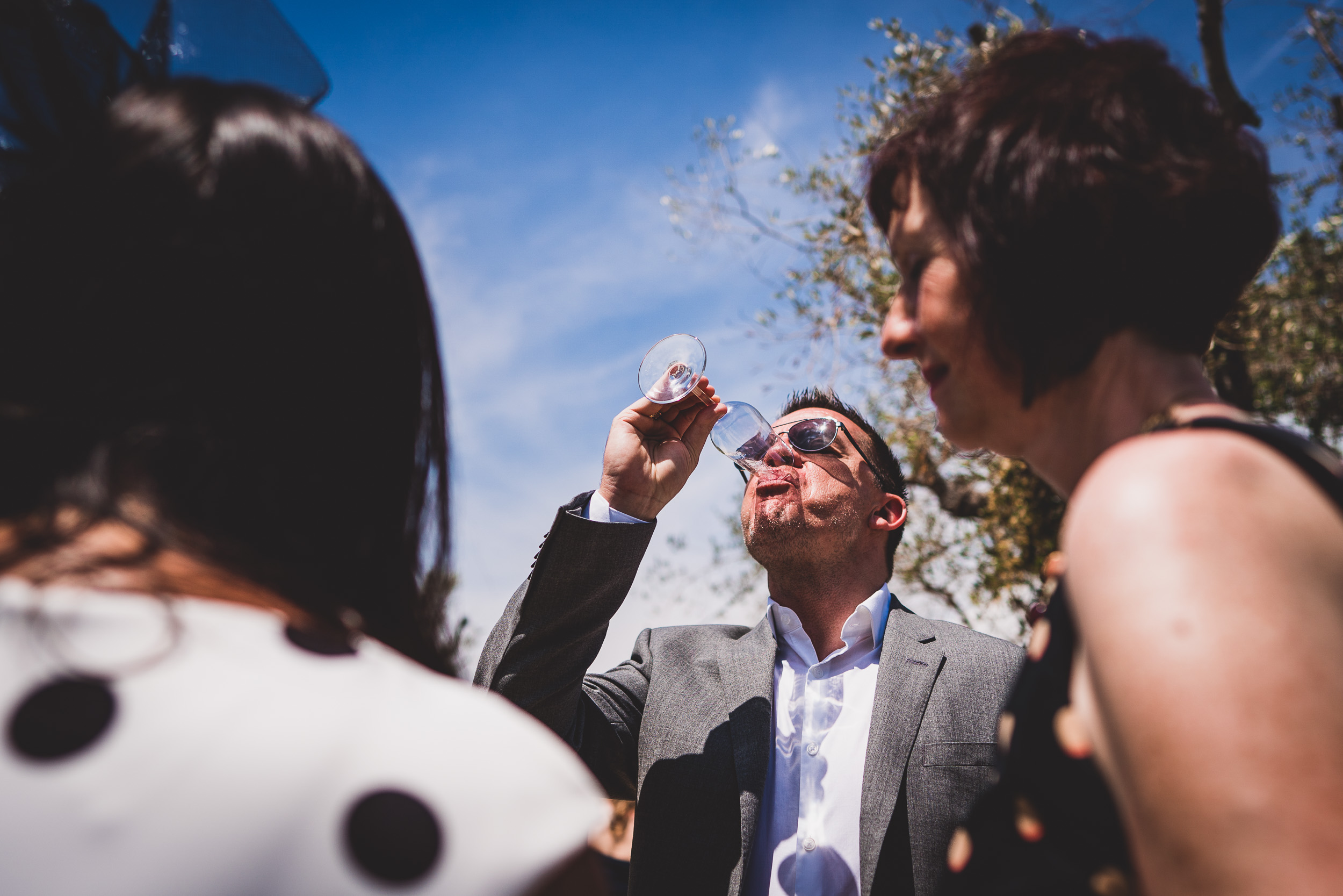 A groom in a suit is holding a glass of wine at his wedding.