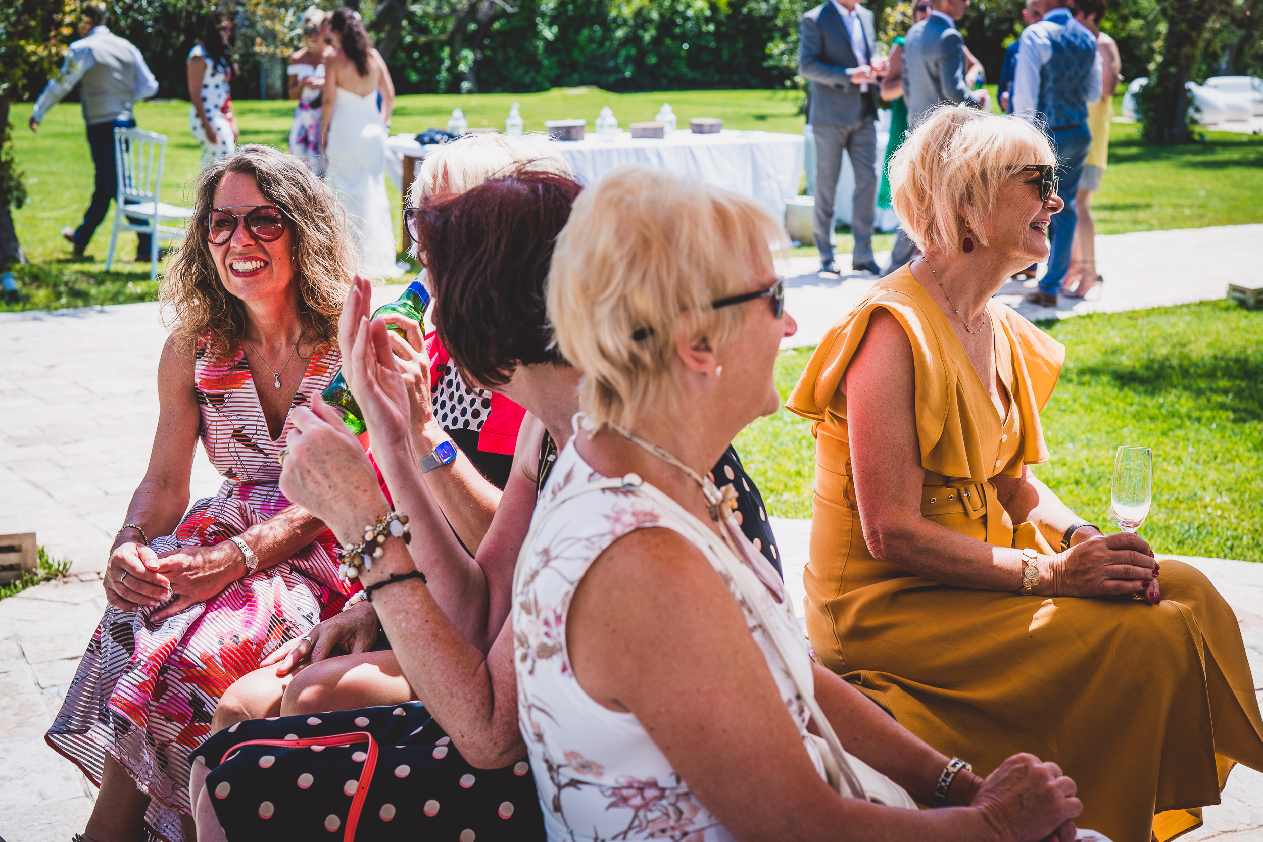 A group of women are sitting in a garden watching a wedding ceremony.