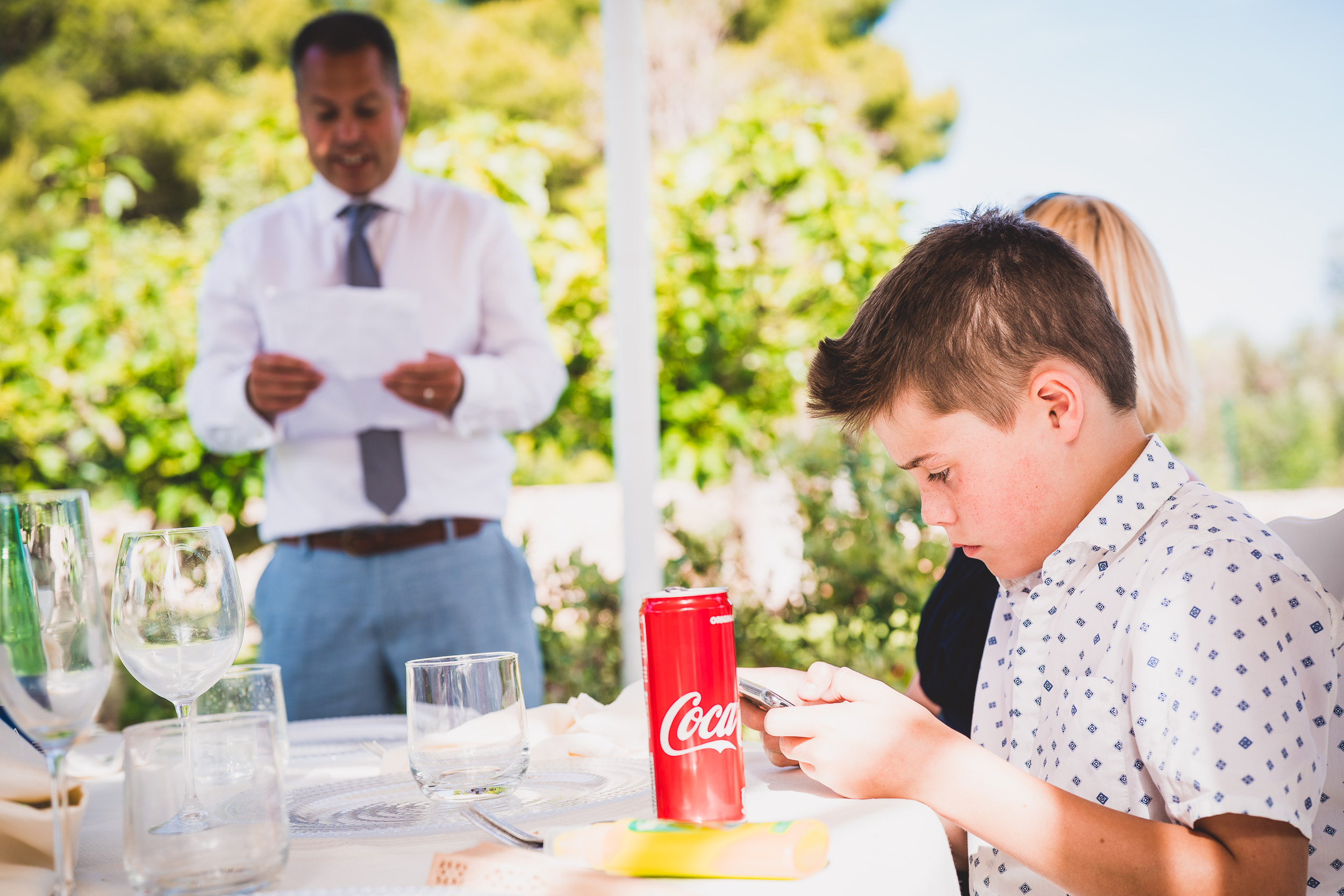 A wedding photographer captures a boy at a table with a coca cola during the wedding.