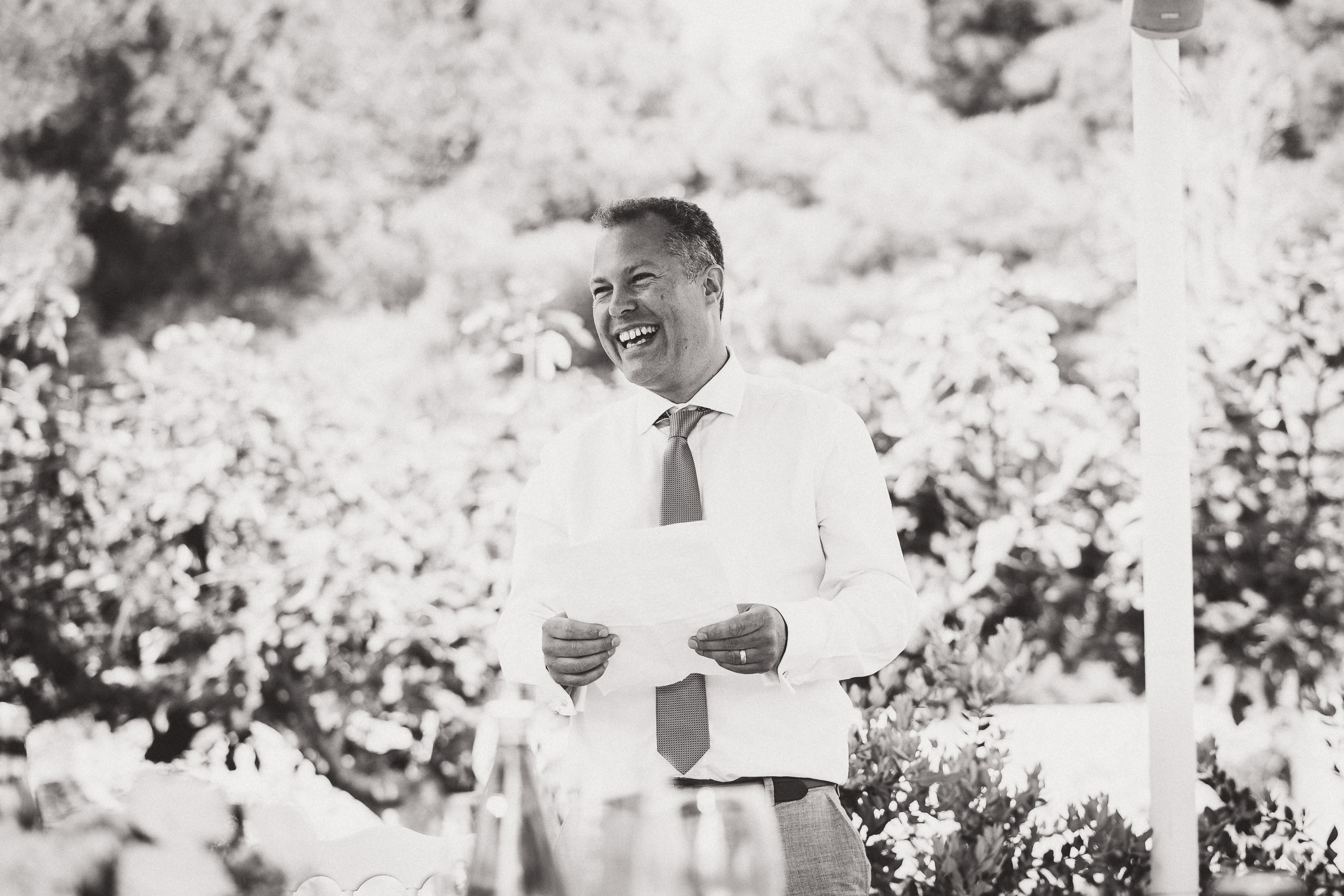 A black and white wedding photo featuring a man giving a speech at the reception.