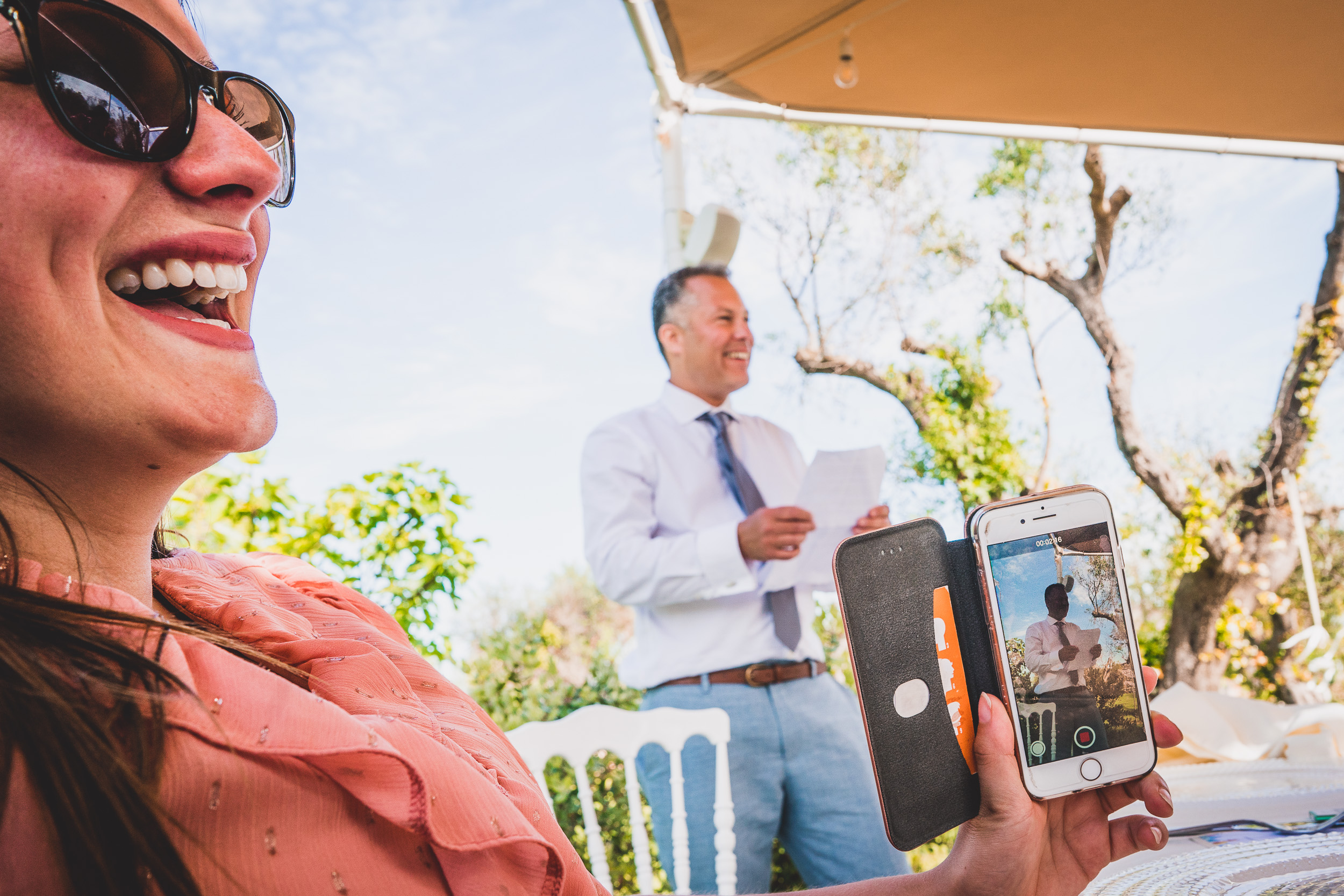 A smiling woman captured in a wedding photo while holding a cell phone.