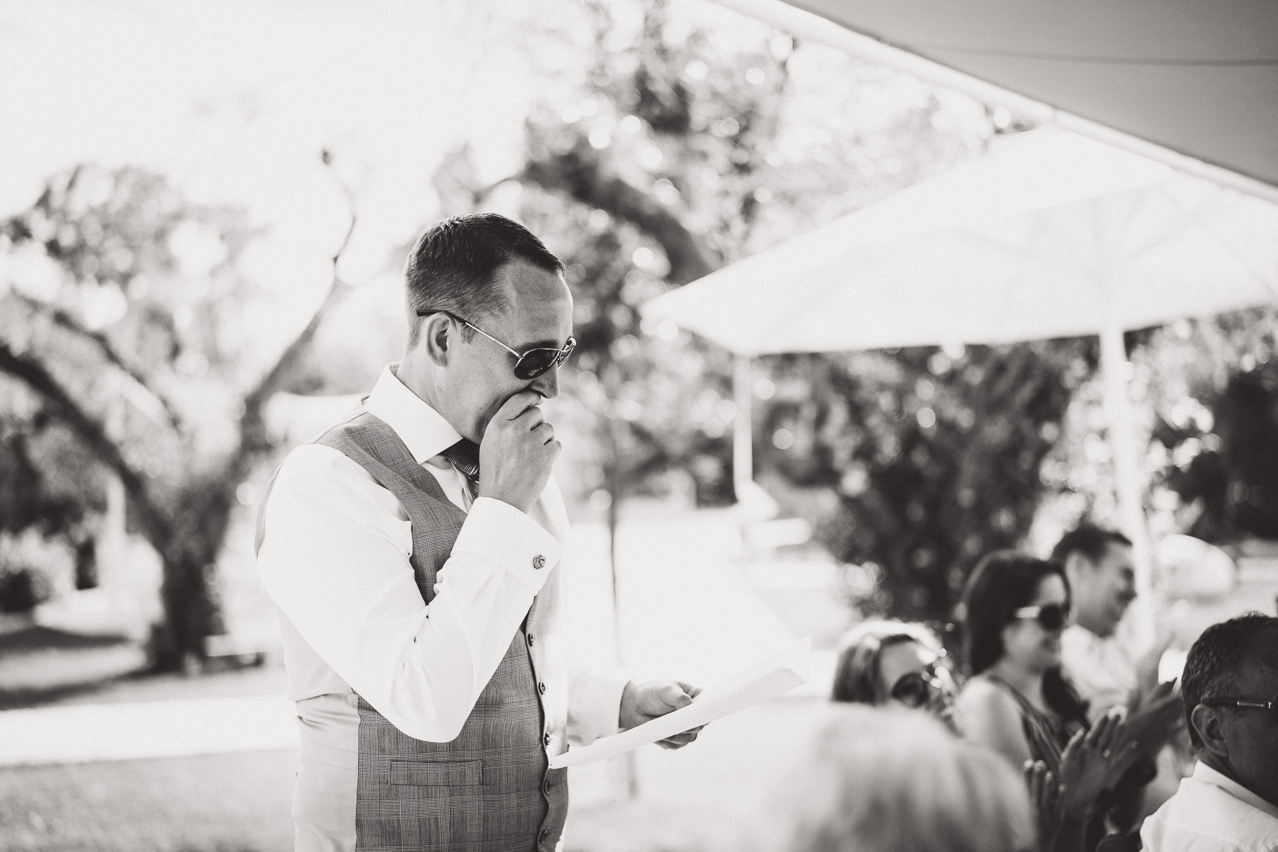 A wedding photographer captures a black and white photo of a man giving a speech at a wedding.