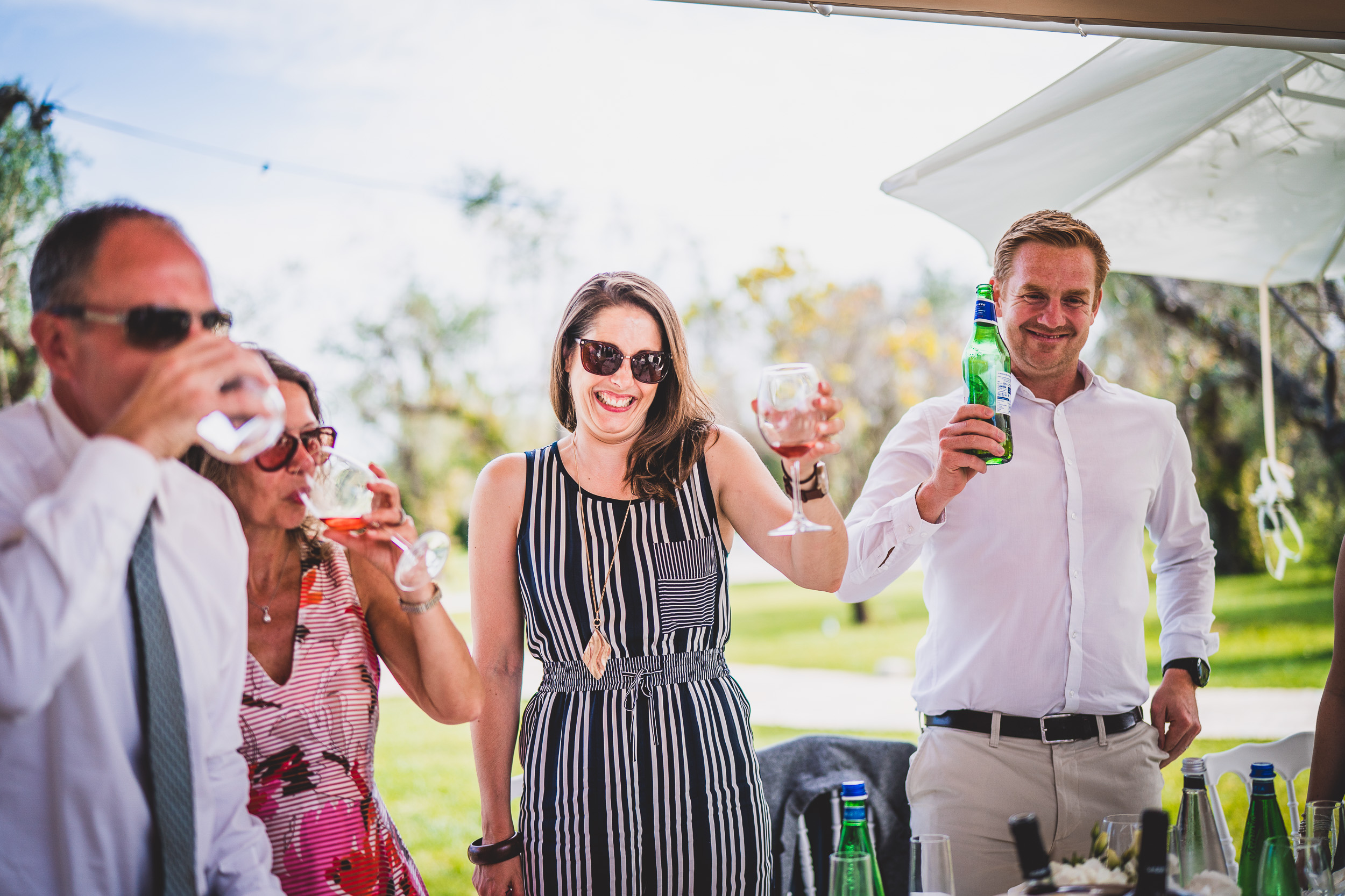 A group of people celebrating at an outdoor wedding event, with wine being enjoyed.