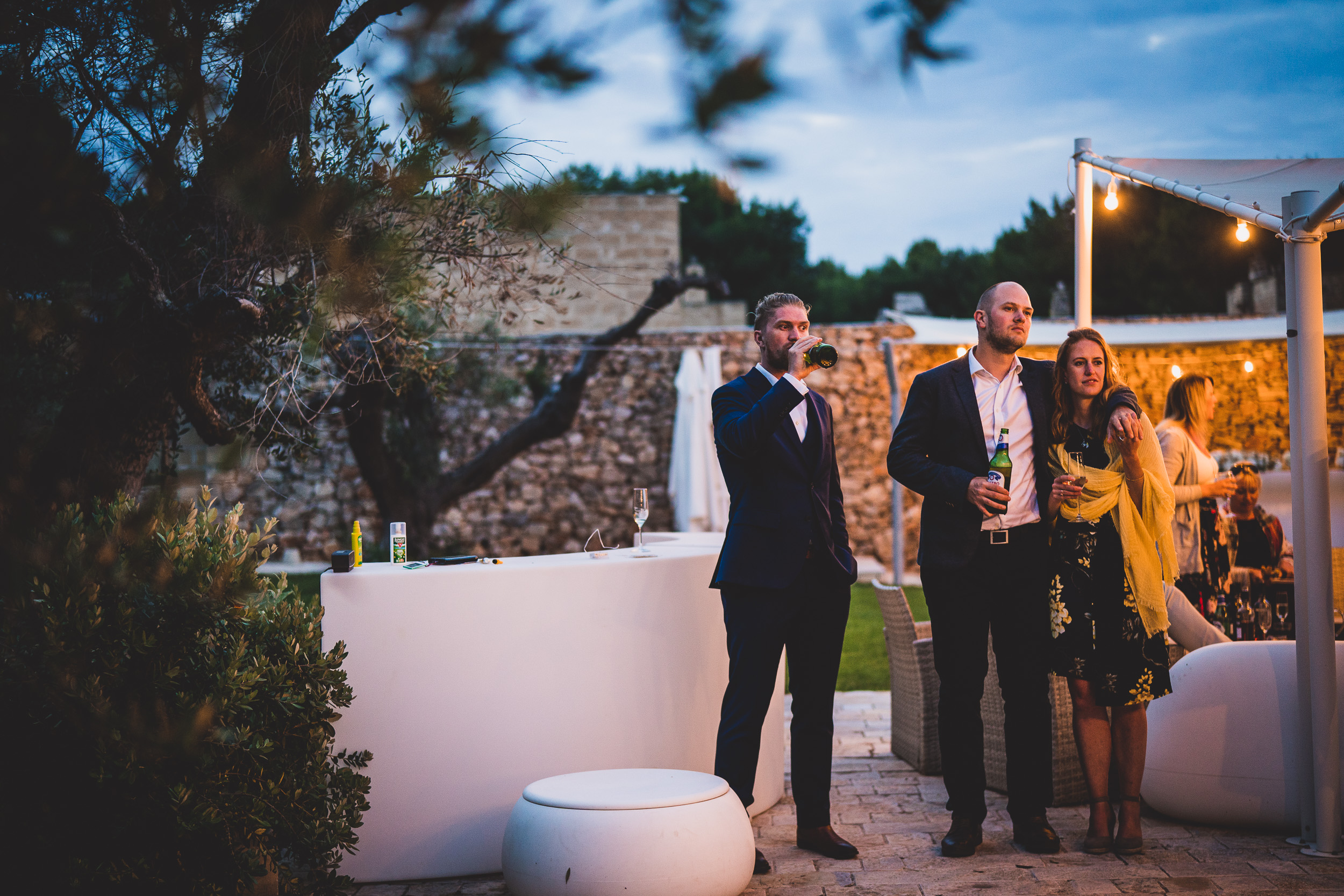 A group of people posing for a wedding photo in front of an outdoor area.