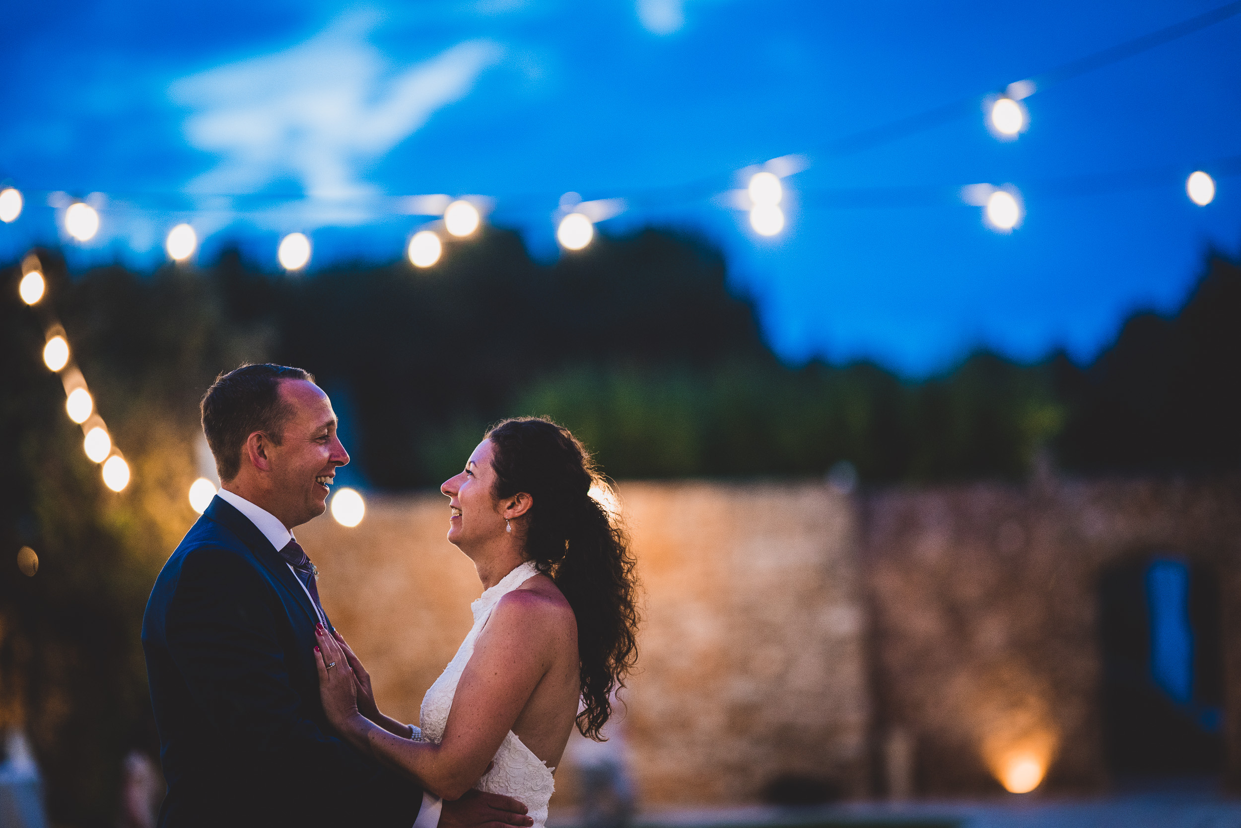 A groom and bride captured by a wedding photographer with a stunning string of lights in the background.