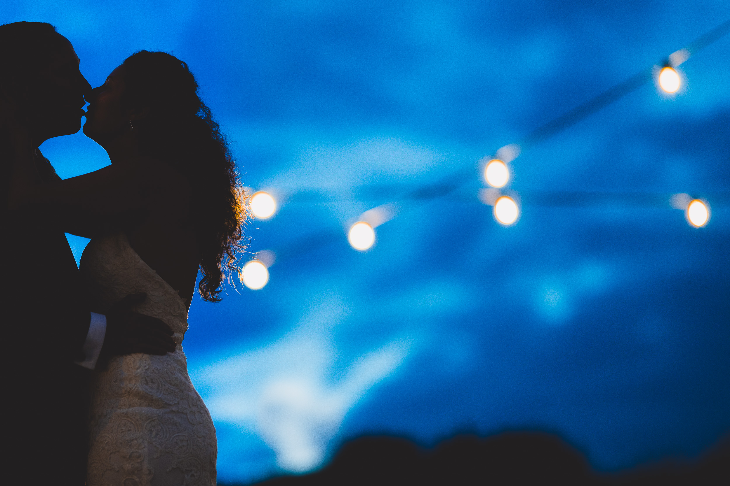 A bride and groom share a romantic kiss under enchanting string lights, captured by a talented wedding photographer.