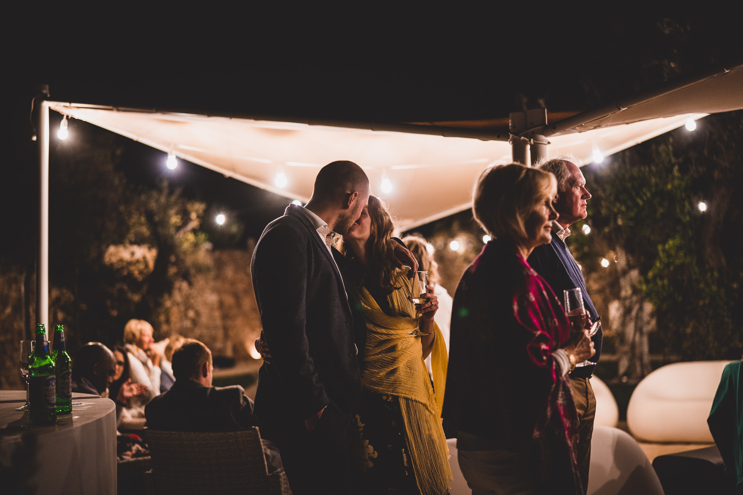 A bride and groom sharing a romantic kiss under a tent at night in a beautiful wedding photo.