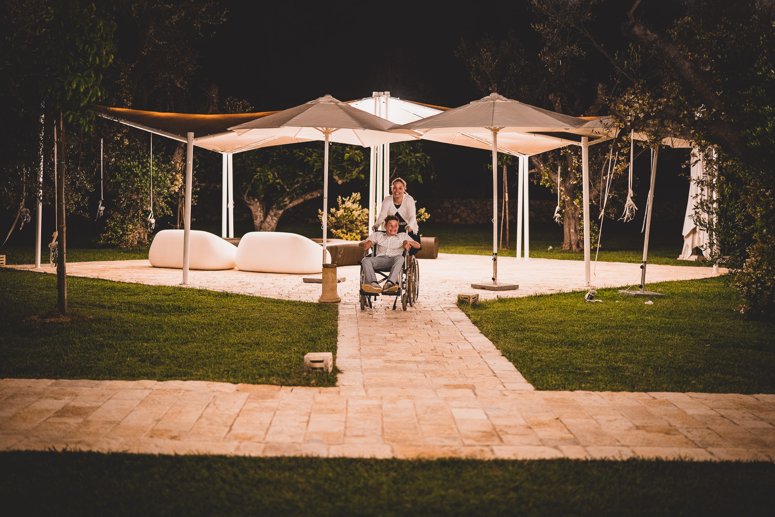 A groom in a wheelchair during a wedding photo session in a garden at night.