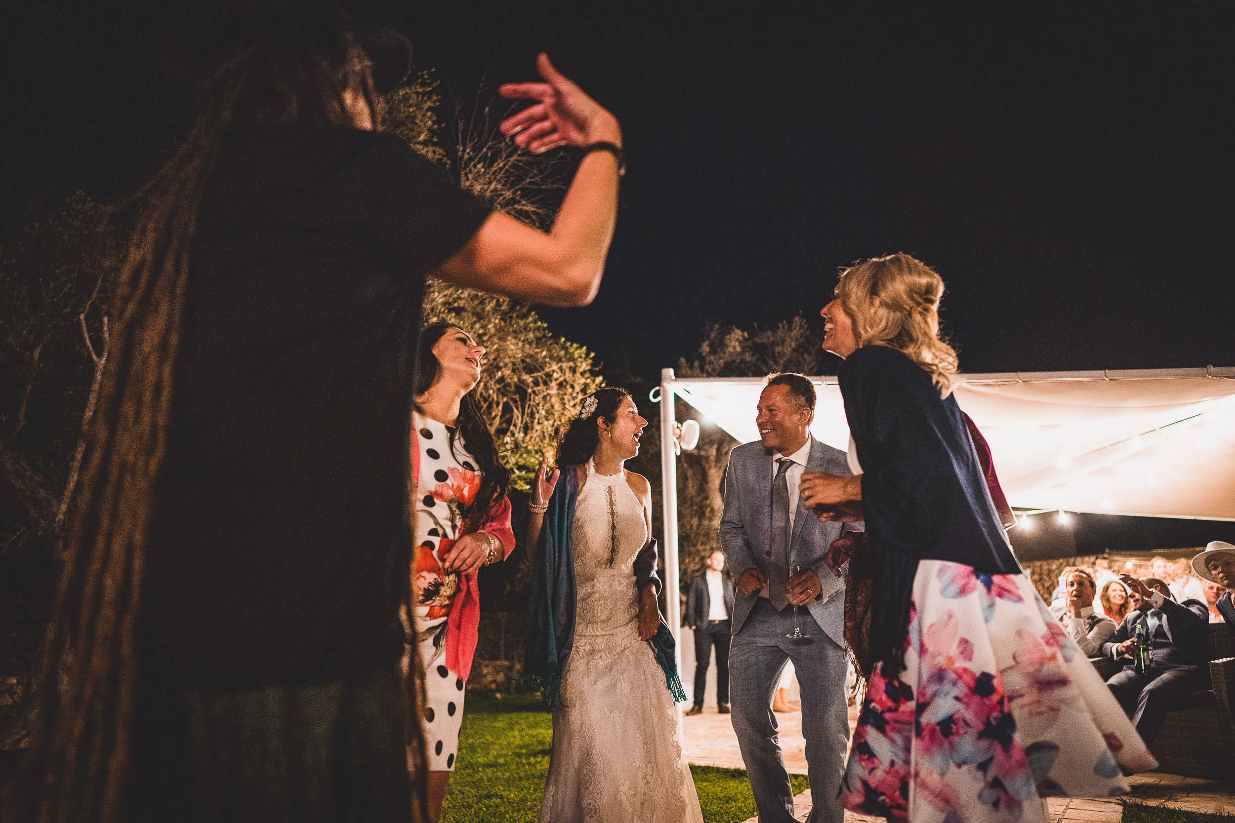 A group of people celebrating at a wedding, dancing in a garden at night.