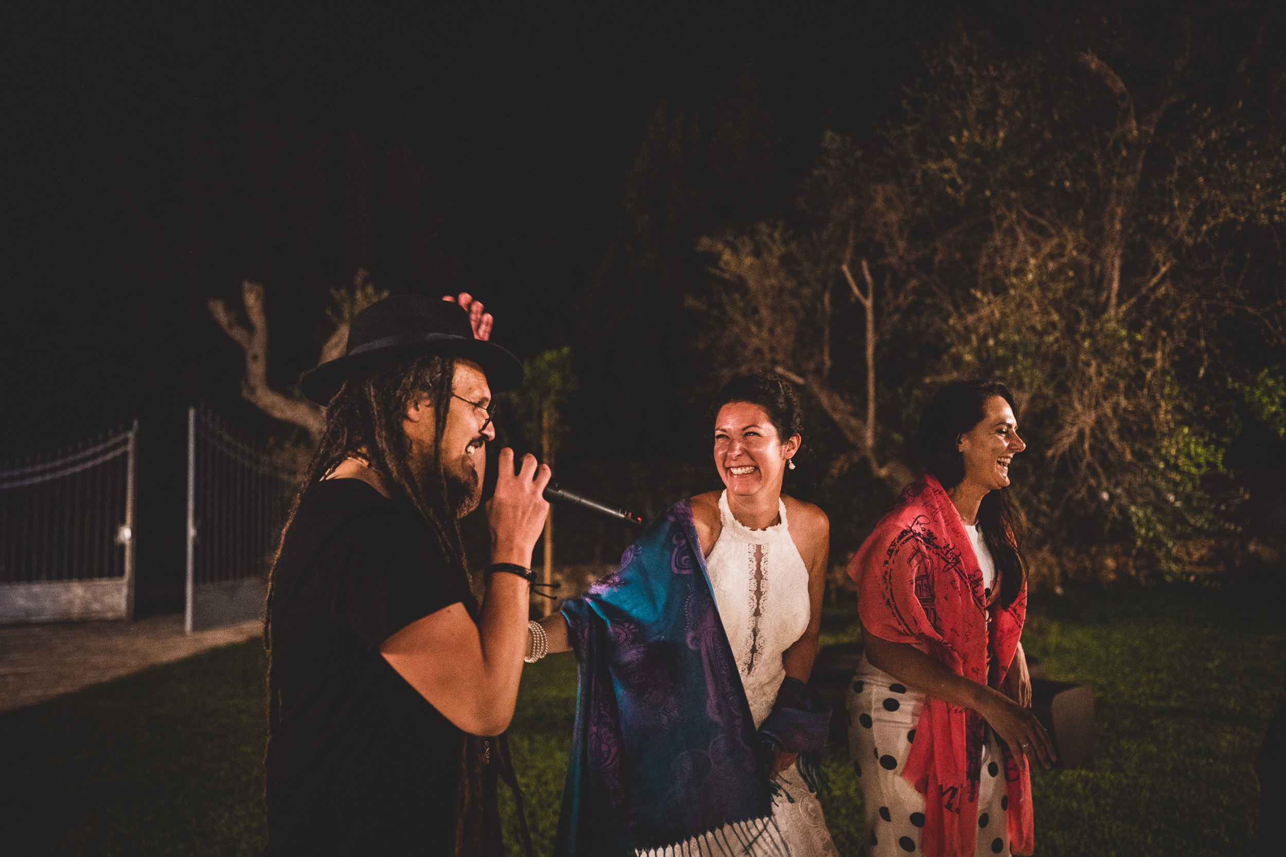 A group of people, including the bride and groom, standing in a yard with a microphone for their wedding photo.