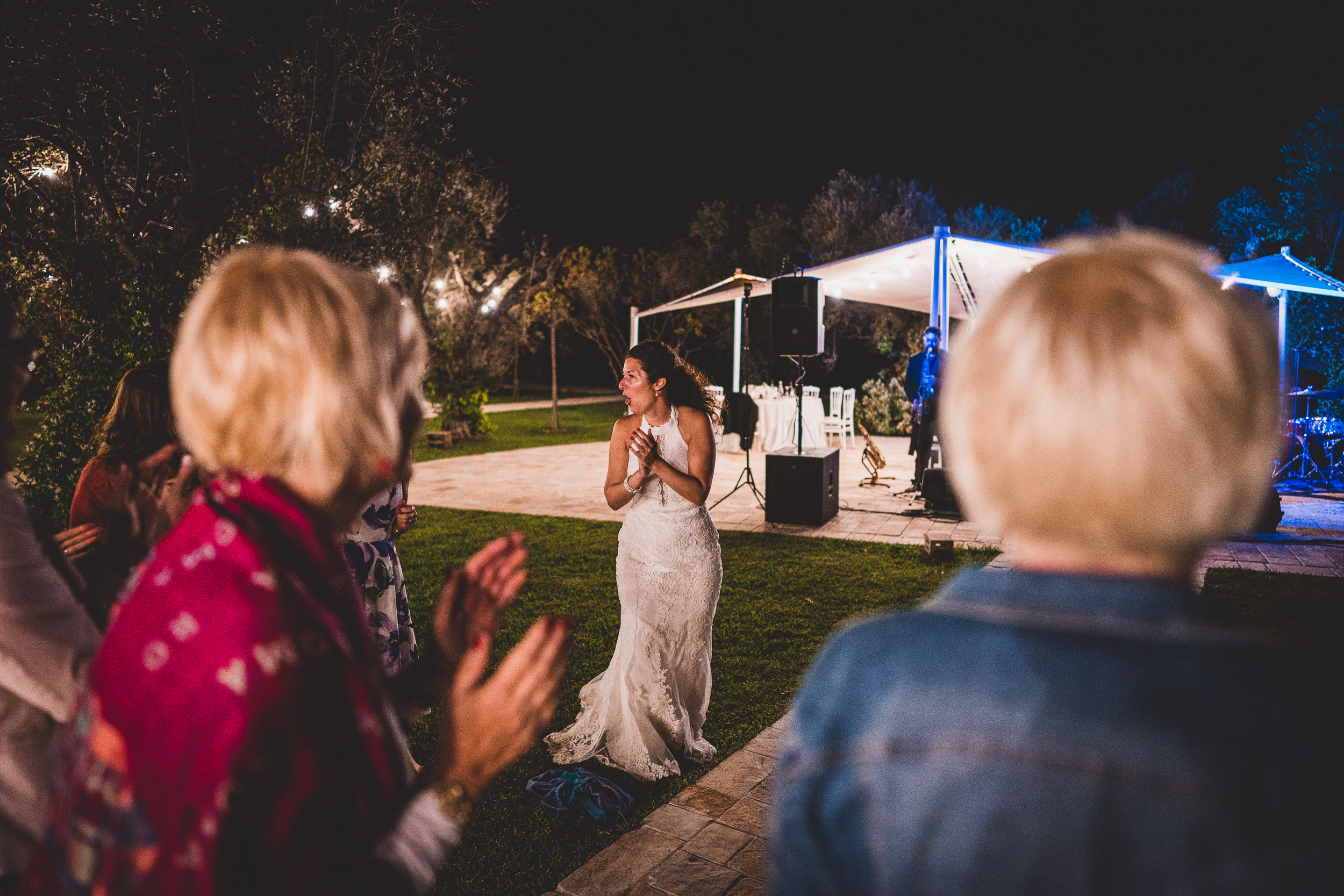 A bride clapping in front of a crowd at her wedding.