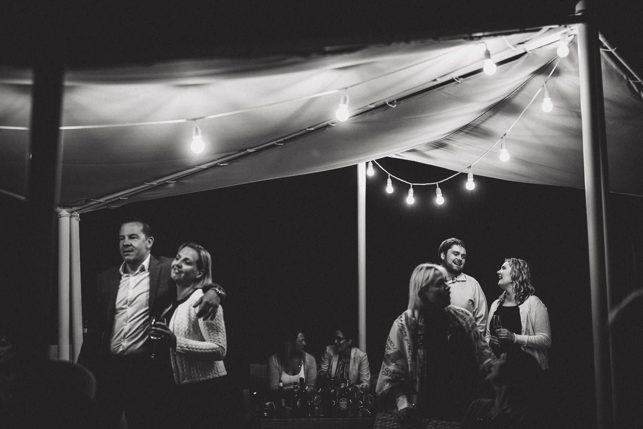 A wedding photographer capturing a group of people under a tent at night.