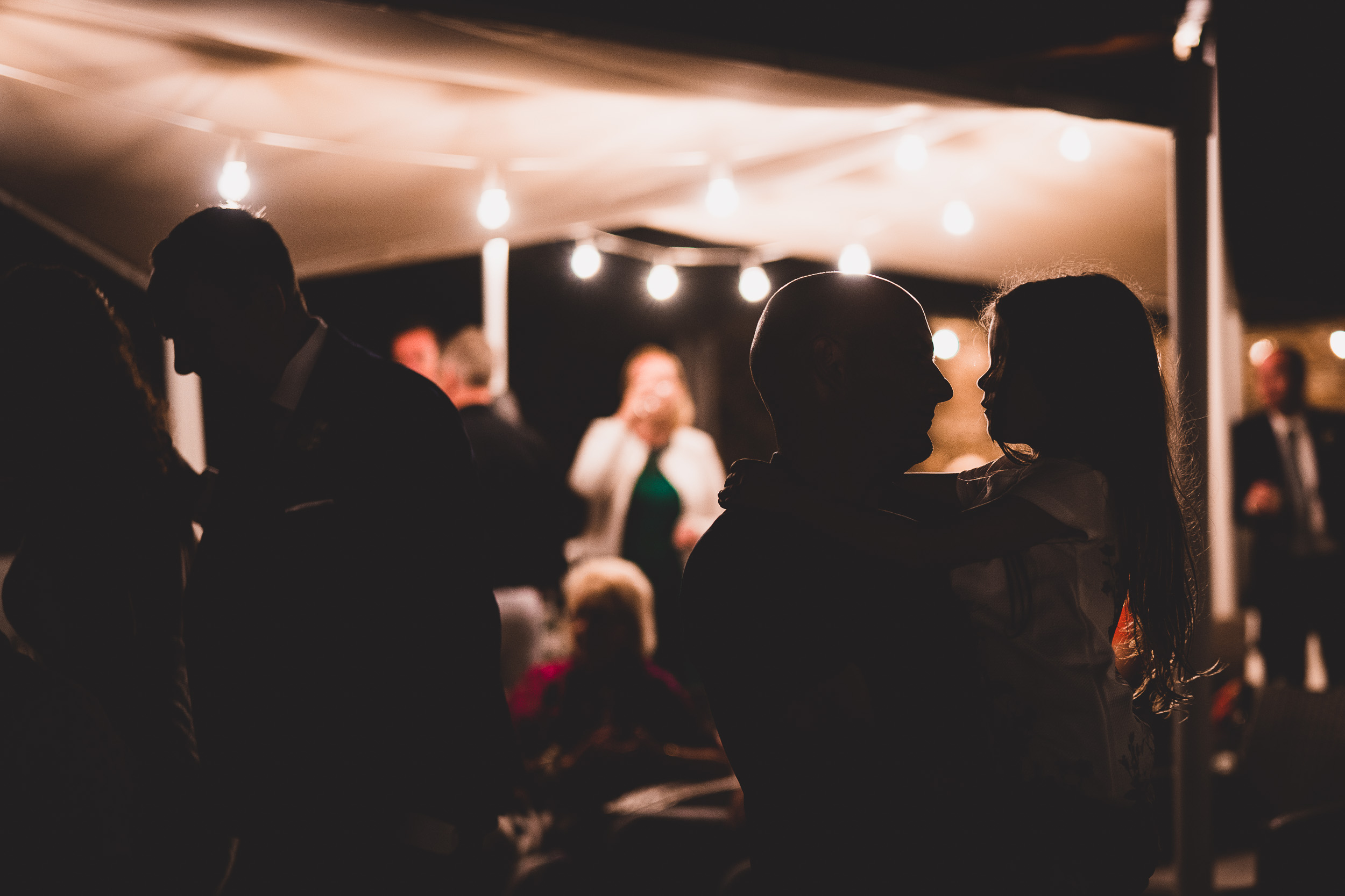 A bride and groom pose for their wedding photographer inside a tent at night.