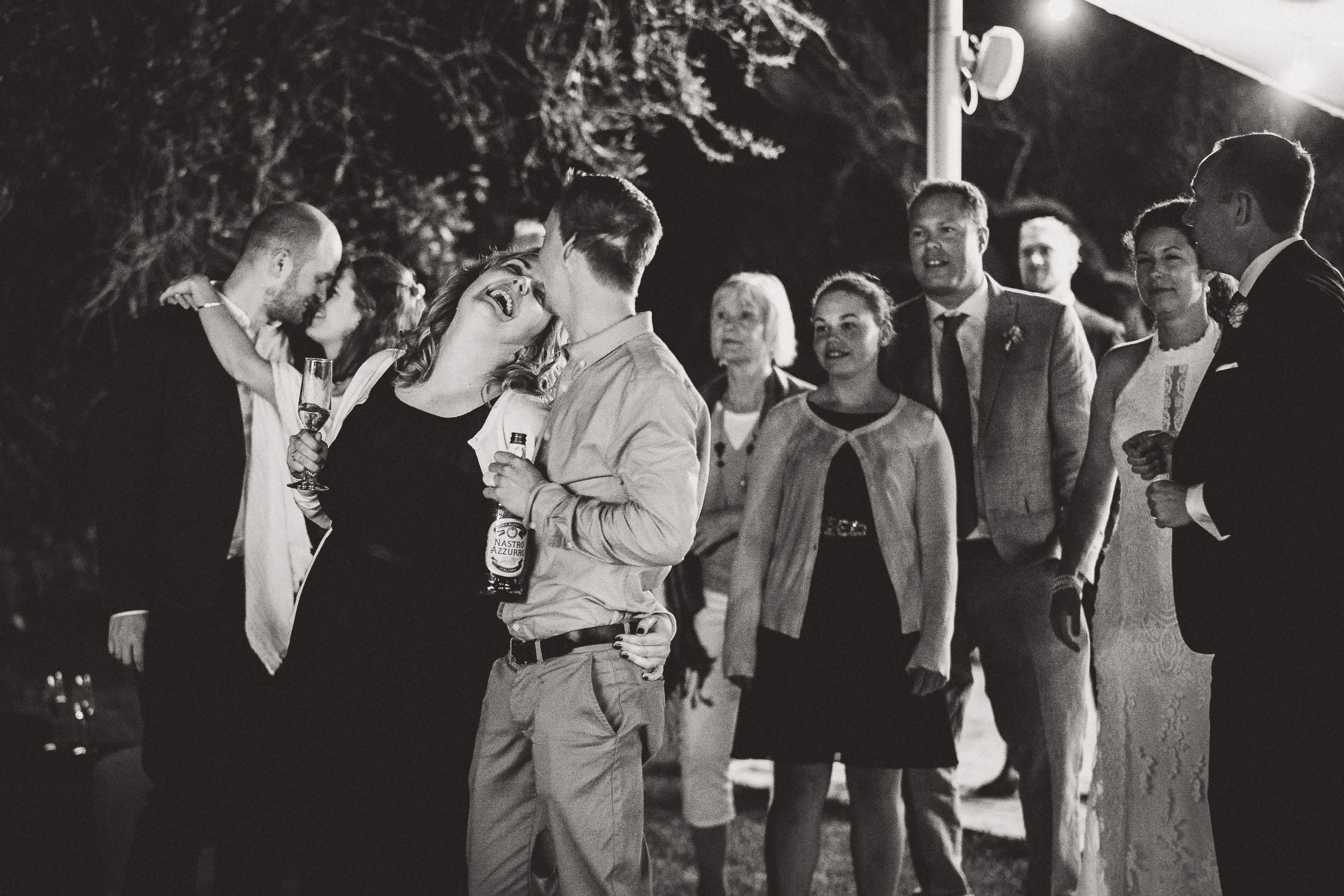 A black and white photo capturing a group of people at a wedding, including the bride and groom.