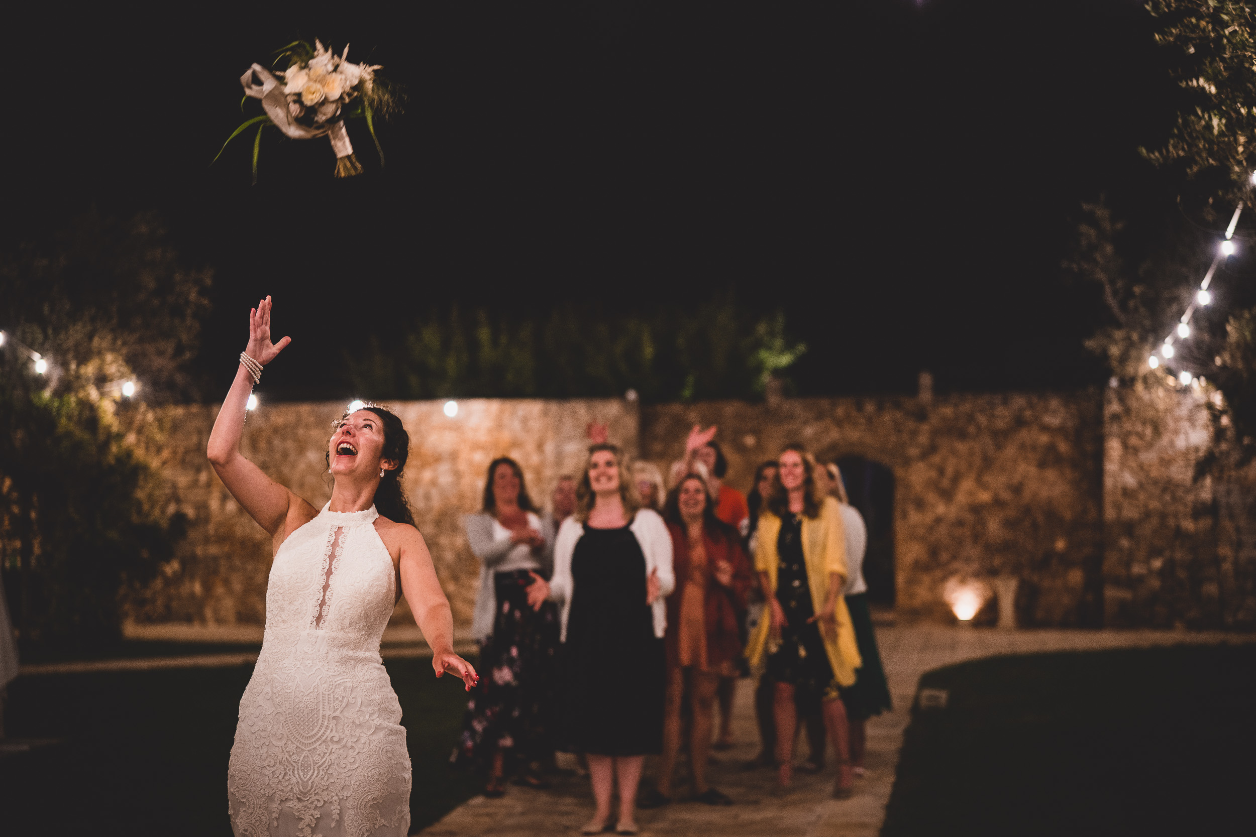 A bride throwing bouquet to bridesmaids during a nighttime wedding.