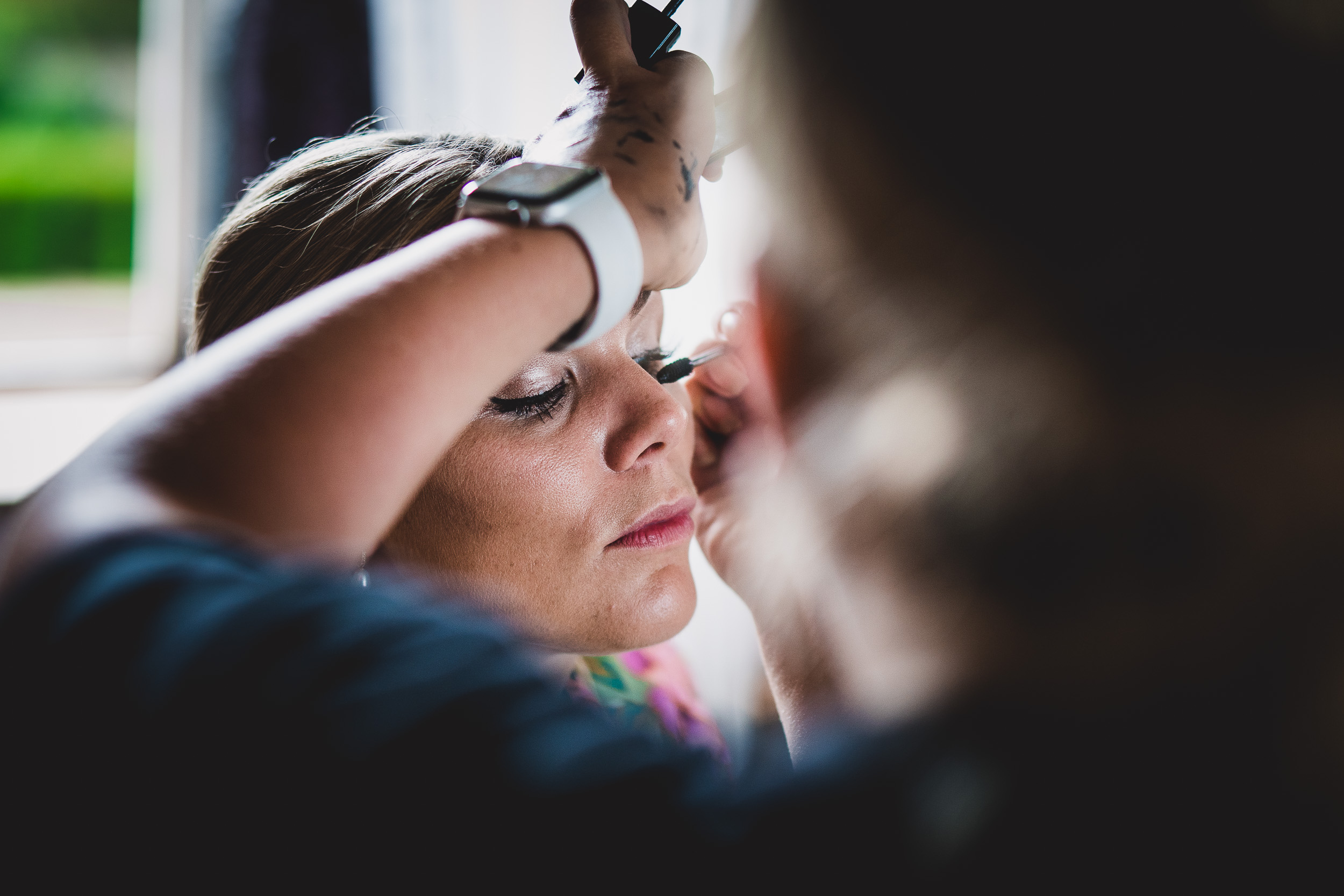 A bride getting her makeup done in front of a mirror for her wedding photo.