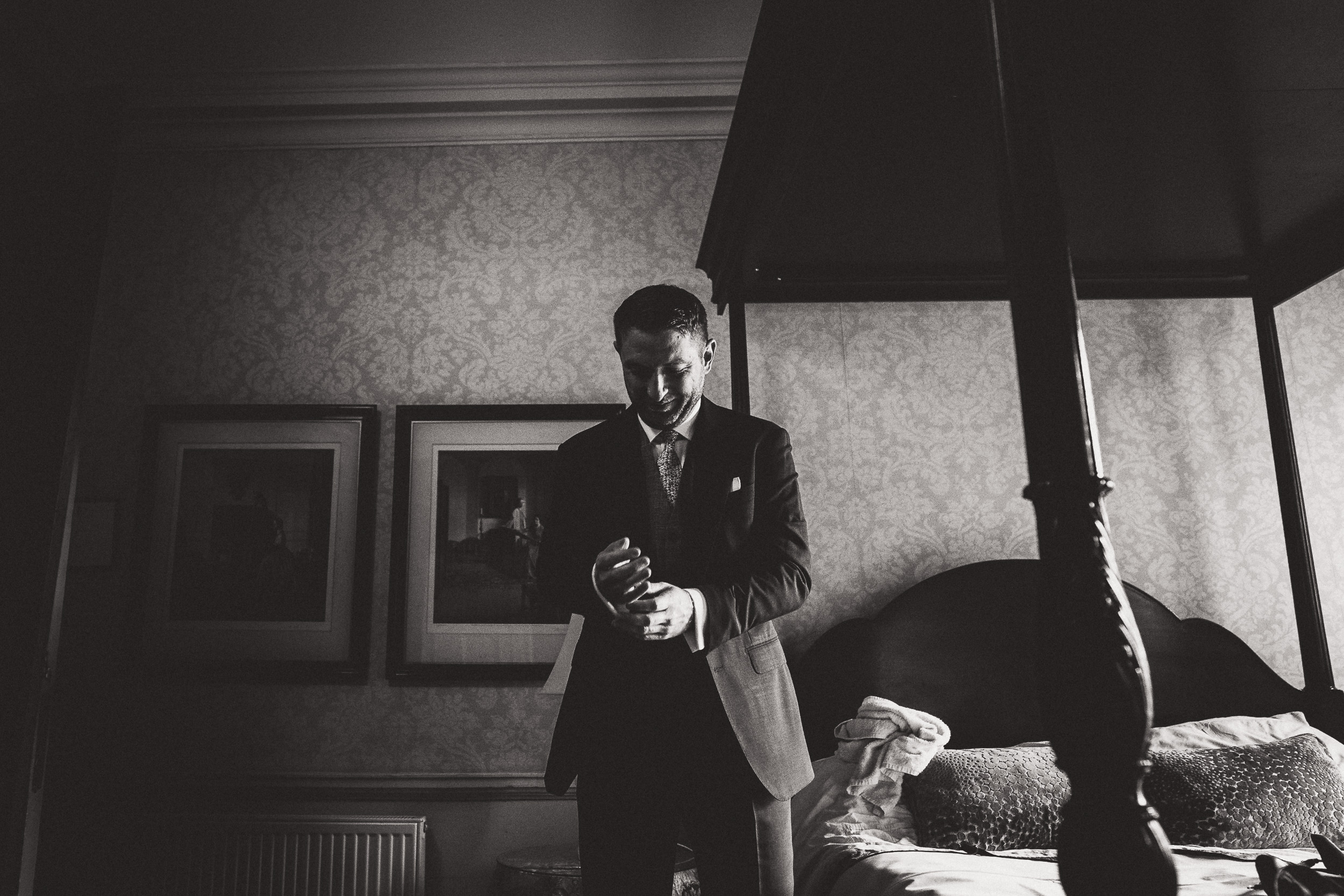 A groom in a suit standing in front of a bed.