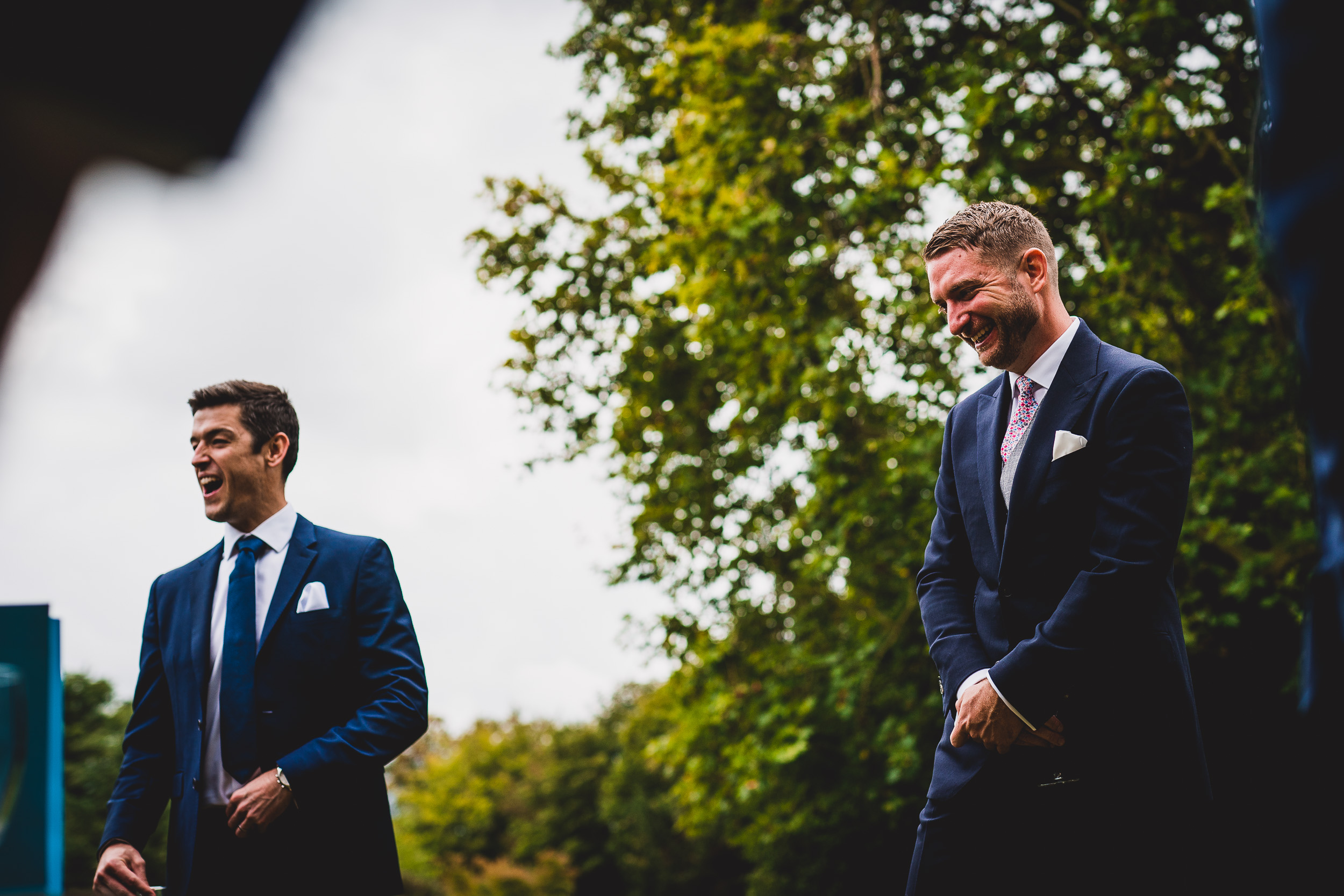 Two men in suits standing next to each other at a wedding.