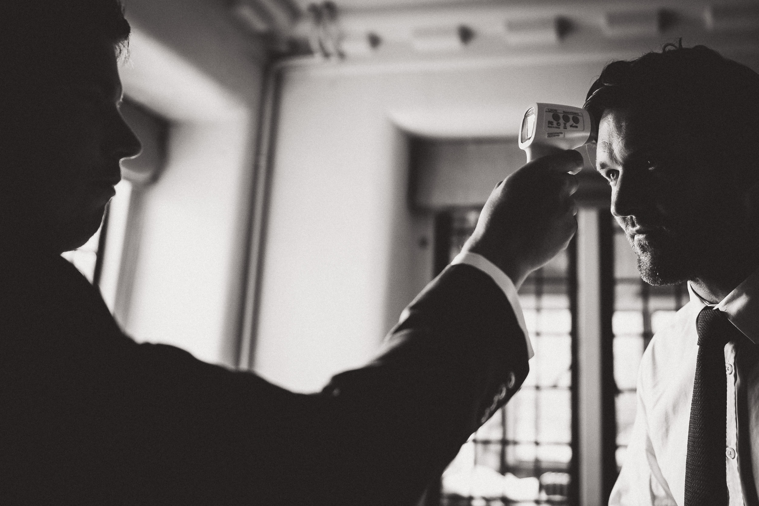 A wedding photographer captures a unique moment as the groom carefully balances a glass of wine on the bride's head during a wedding photo.