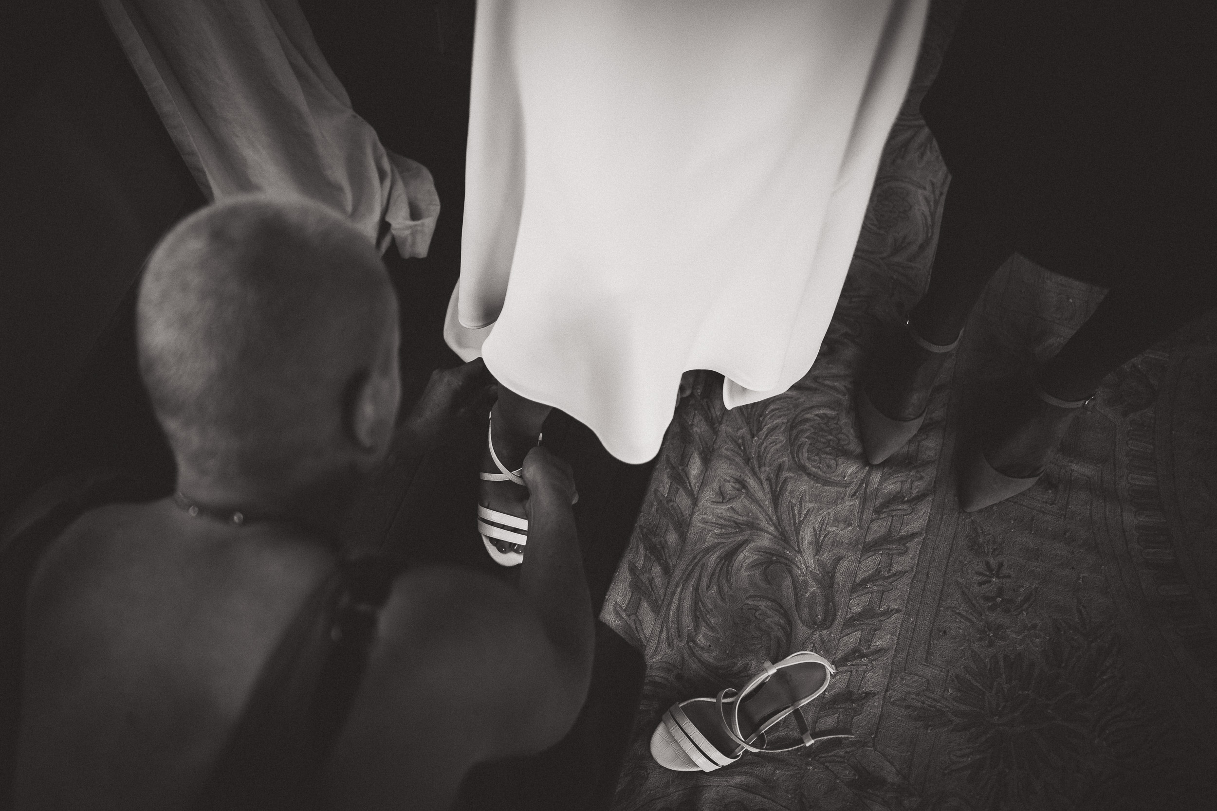 At a wedding, a man is carefully slipping on a bride's shoes for the perfect wedding photo.