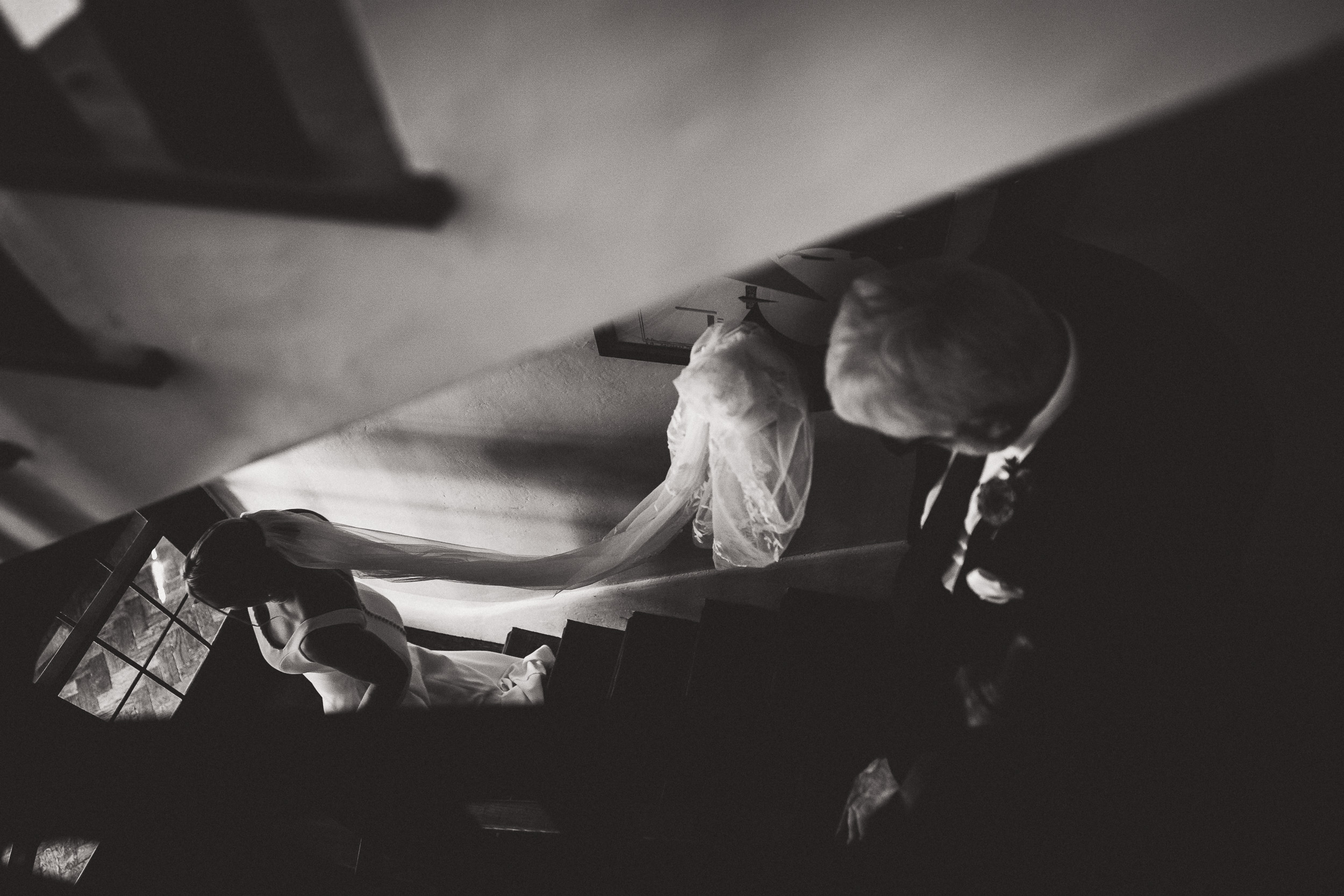 A black and white wedding photo capturing a bride elegantly descending the stairs.