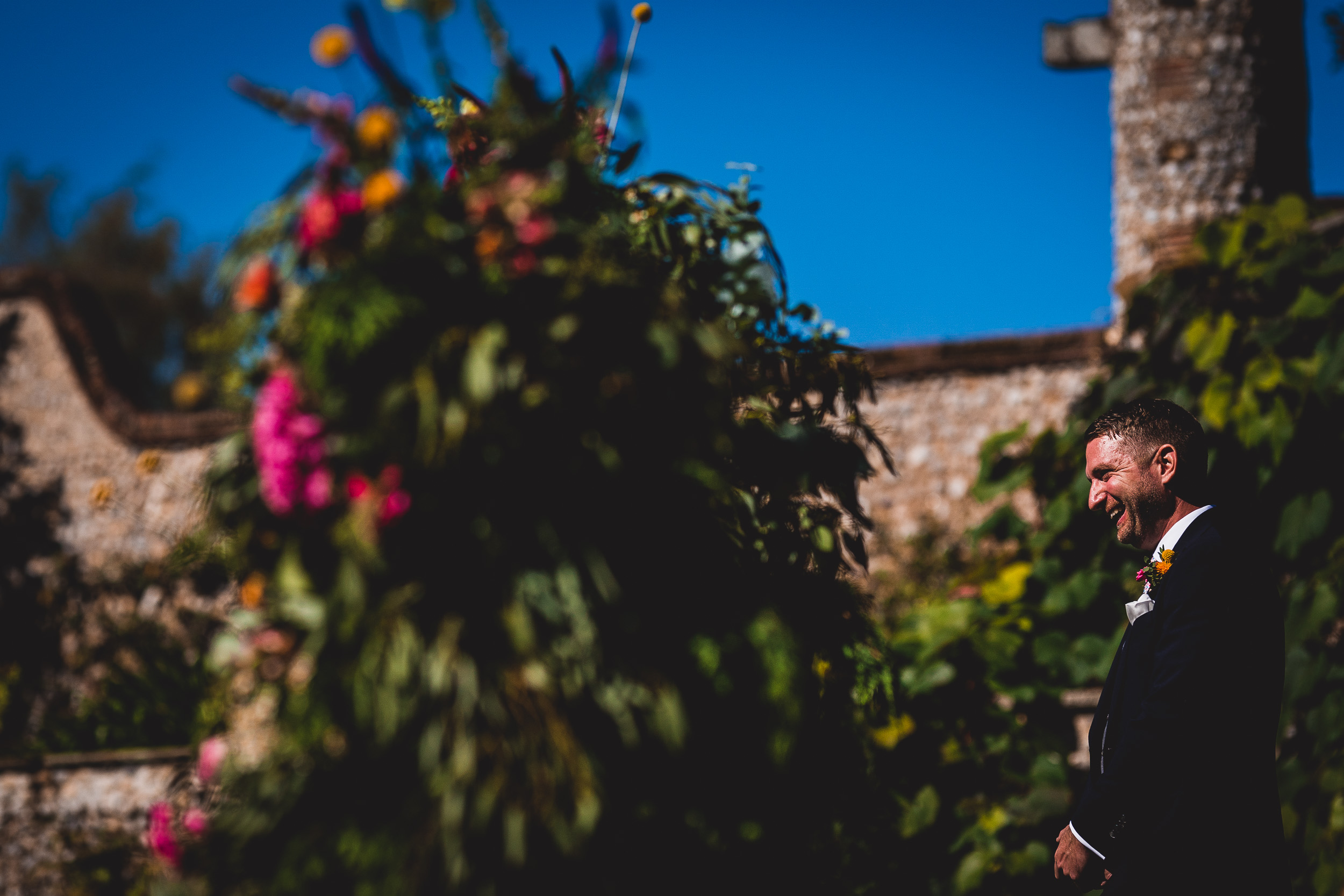 A wedding photographer captures a bride and groom in front of a stone wall.