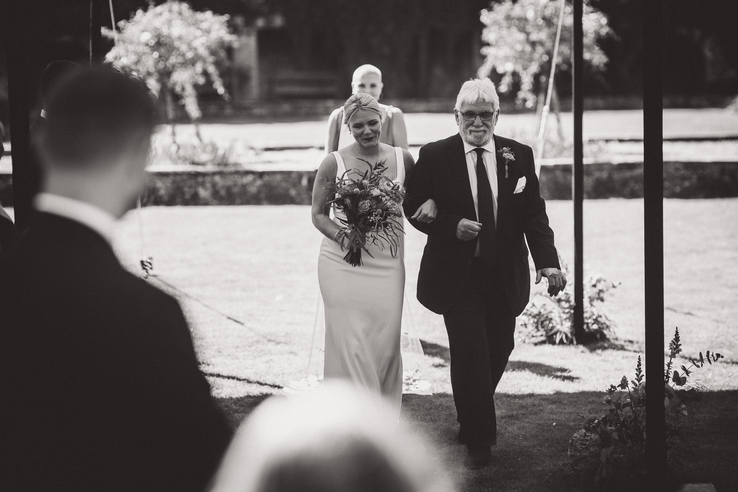 A black and white wedding photo featuring a bride walking down the aisle.