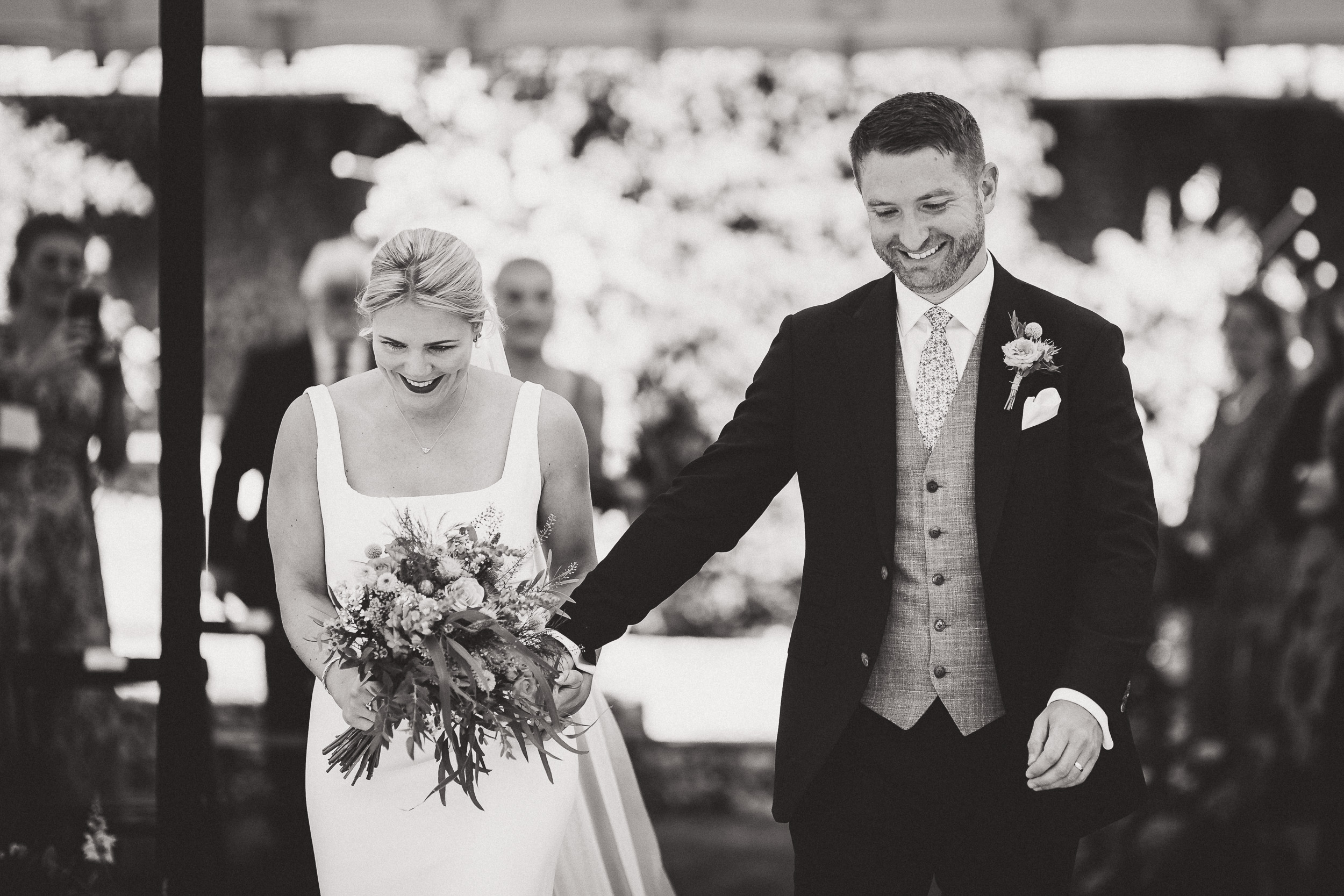 A wedding photographer captures a blissful black and white moment of a bride and groom walking down the aisle.