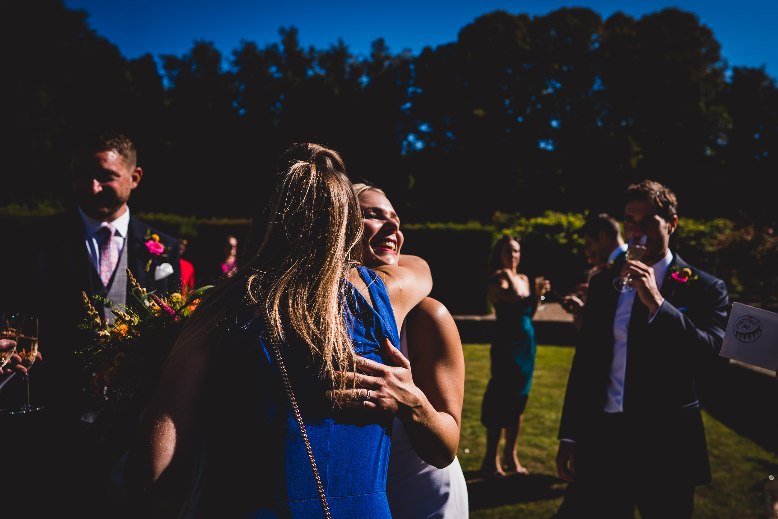 A wedding photographer captures an intimate moment of a groom hugging his bride in a beautiful garden.