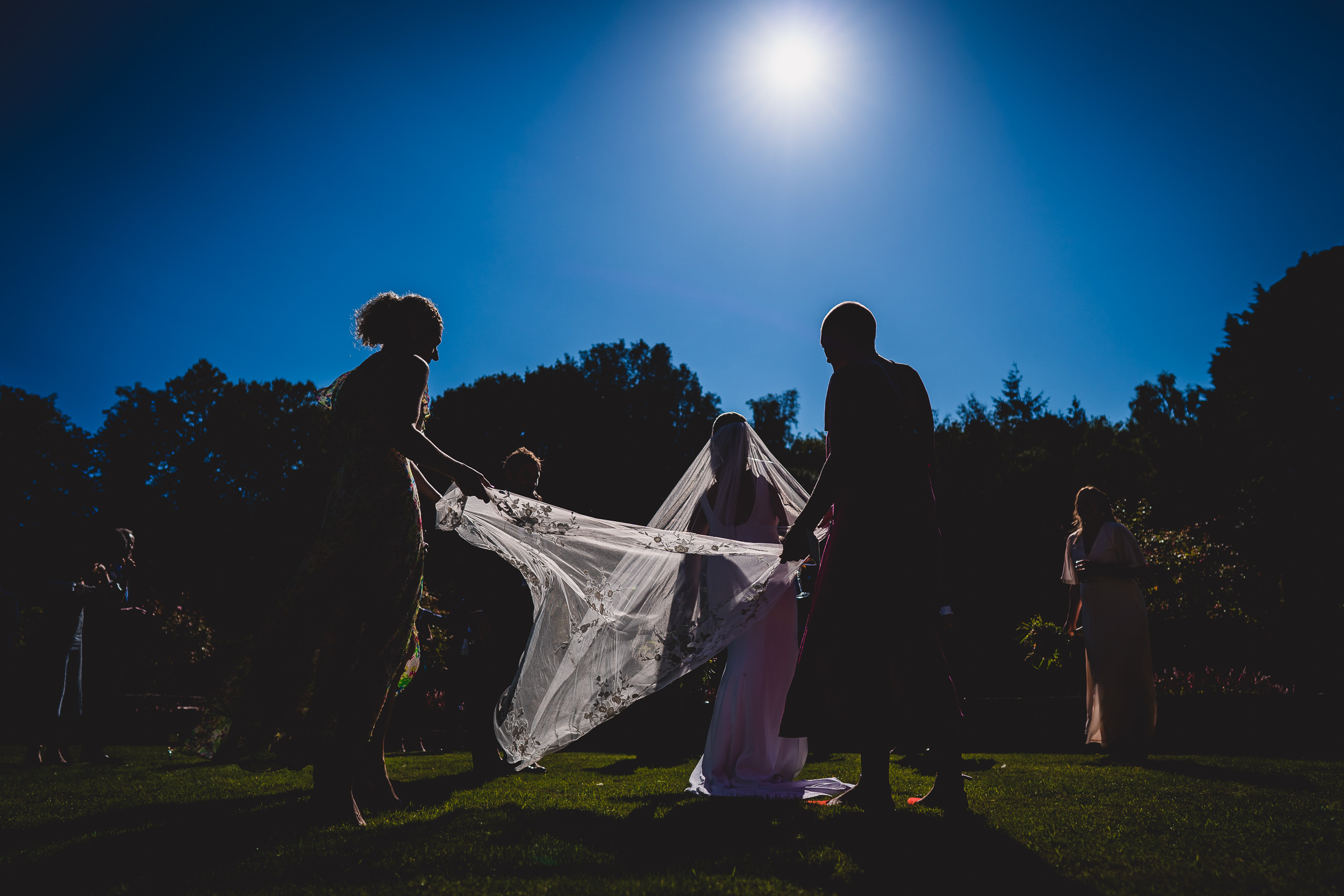 A wedding photographer captures a bride holding her veil in front of the sun.