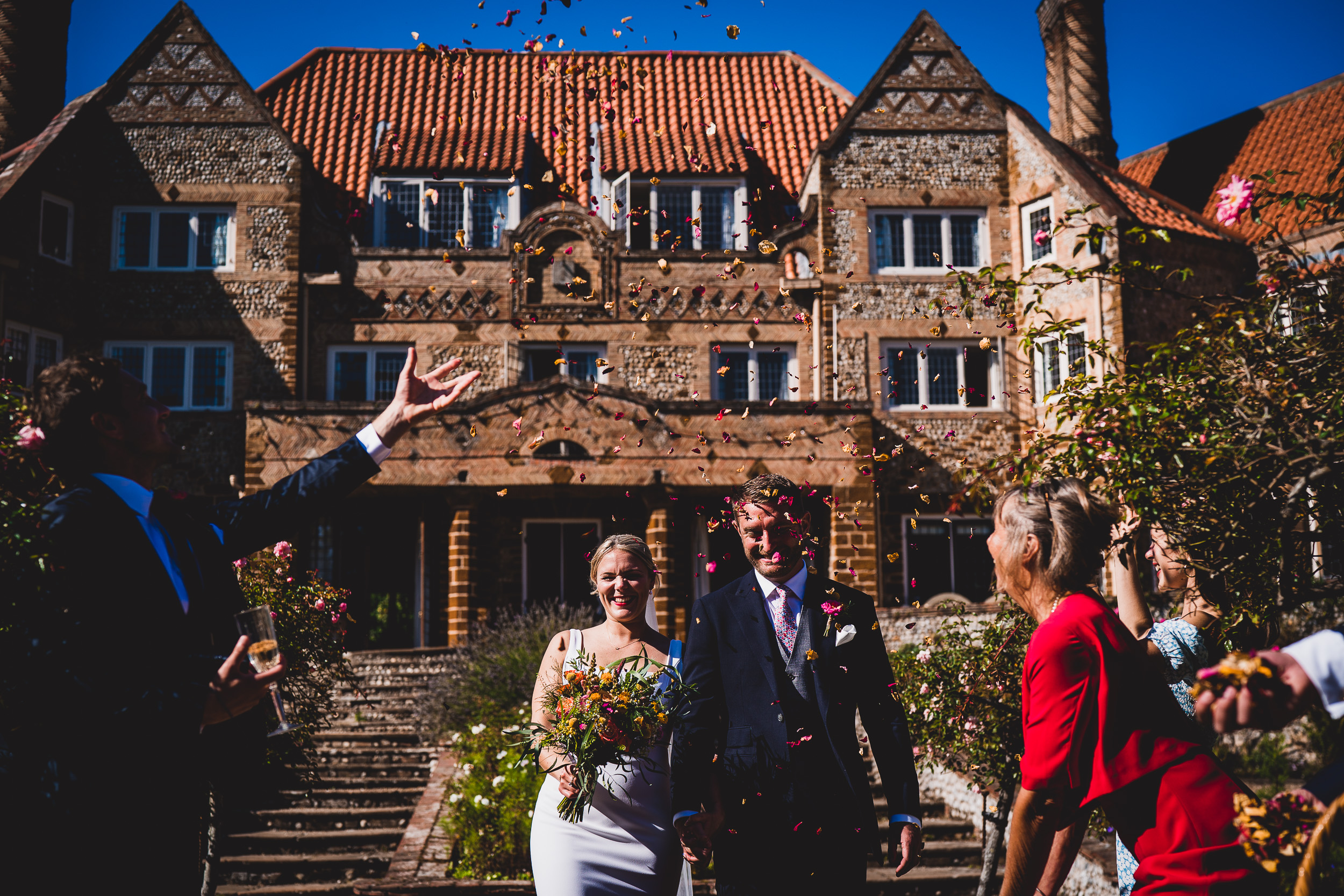 A wedding photo of a bride and groom joyfully throwing confetti in front of a majestic mansion.