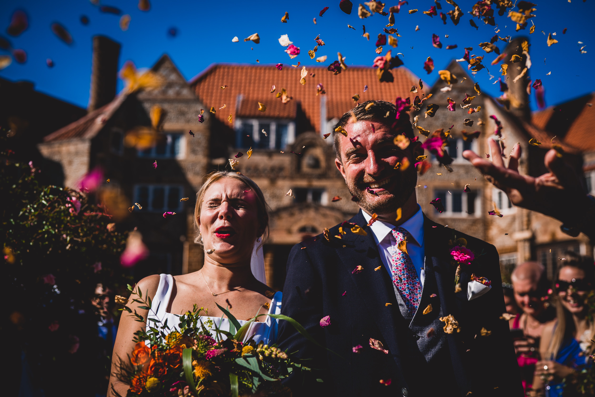 A bride and groom pose for their wedding photo, surrounded by confetti.