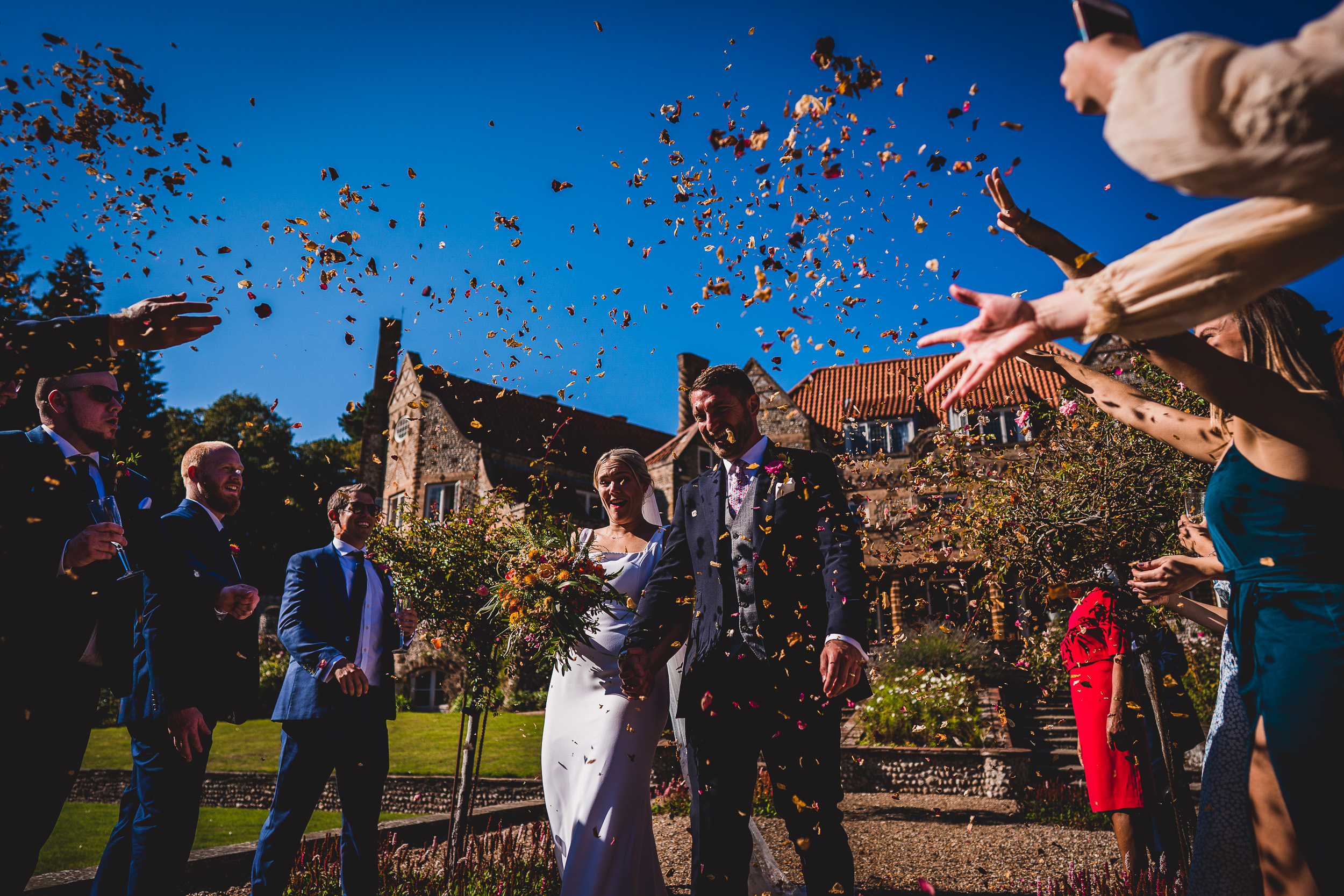 A wedding photographer captures the joyful moment of a wedding party as confetti is thrown.